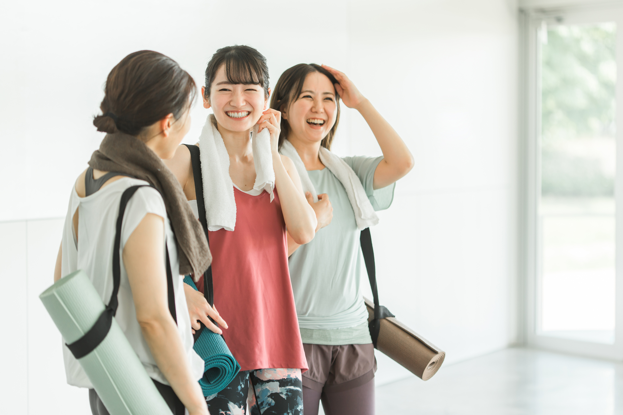 ヨガマットを持ち談笑しているスポーツウェア姿の女性3人
