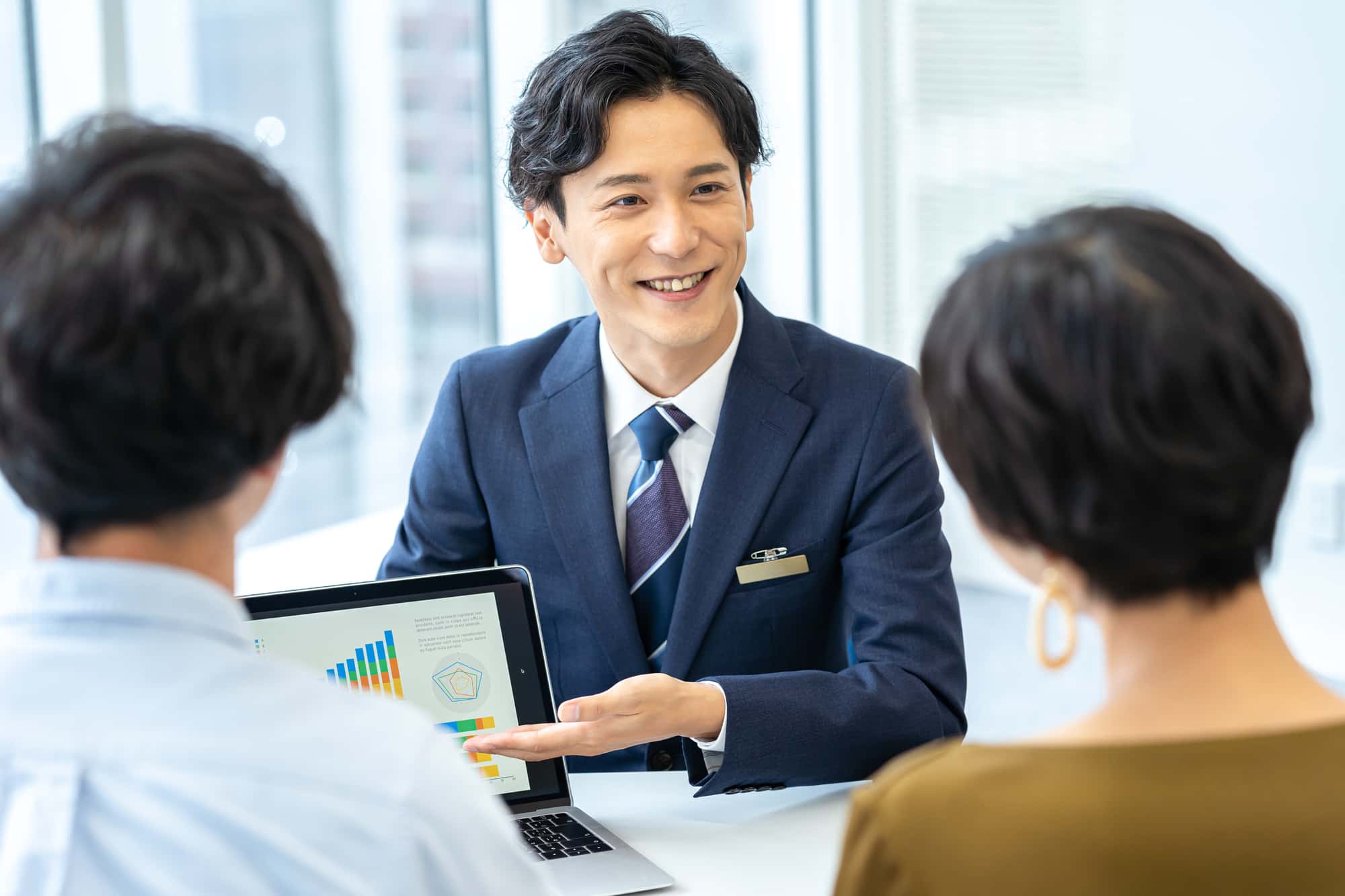 ノートPCの画面を見せながら説明を行うビジネスパーソン