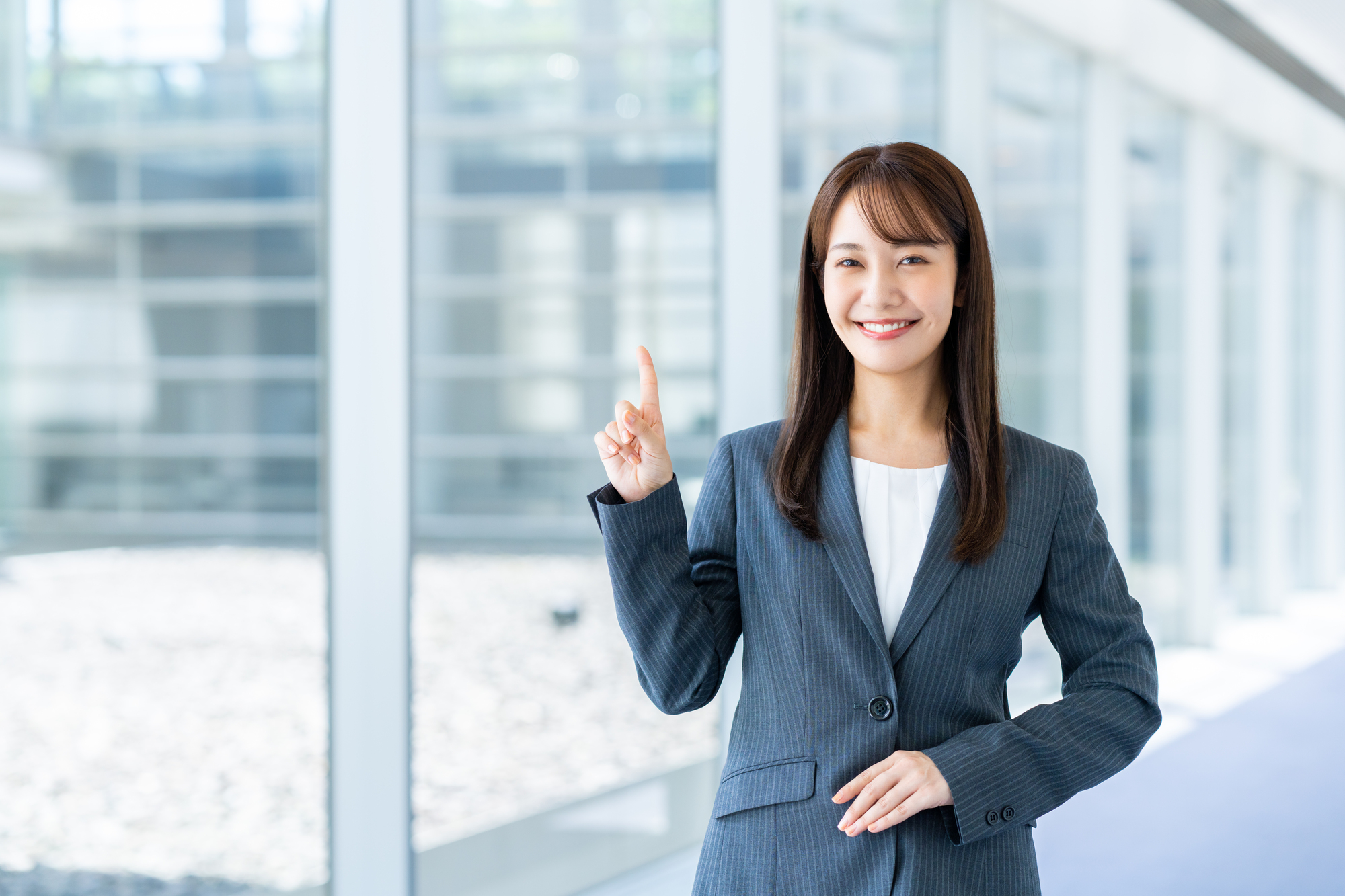人さし指を上に向けて笑顔を浮かべるスーツ姿の女性