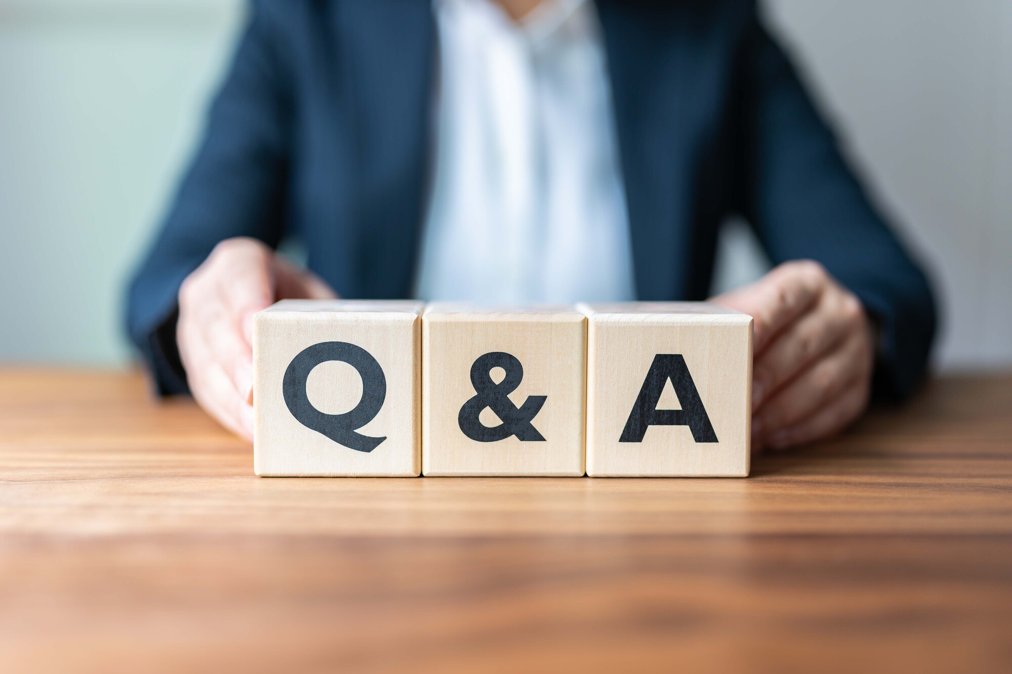 「Q&A」と書かれた木のブロックに手を添えるビジネスパーソン
