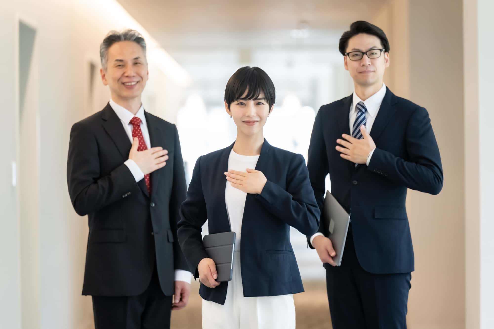 手を胸に当てて笑顔を浮かべる3人のビジネスパーソン