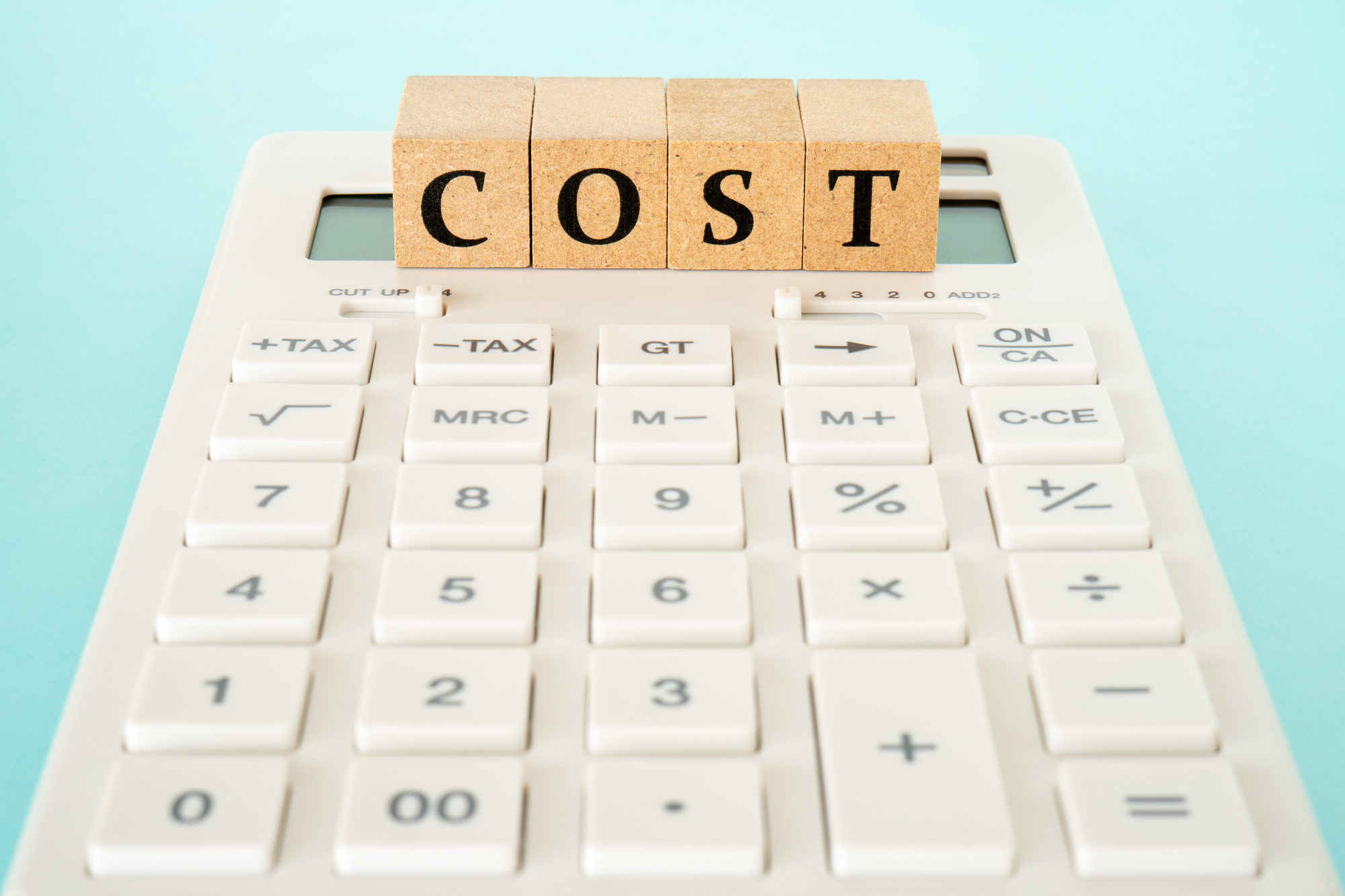 電卓の上に乗った「COST」と書かれた木のブロック