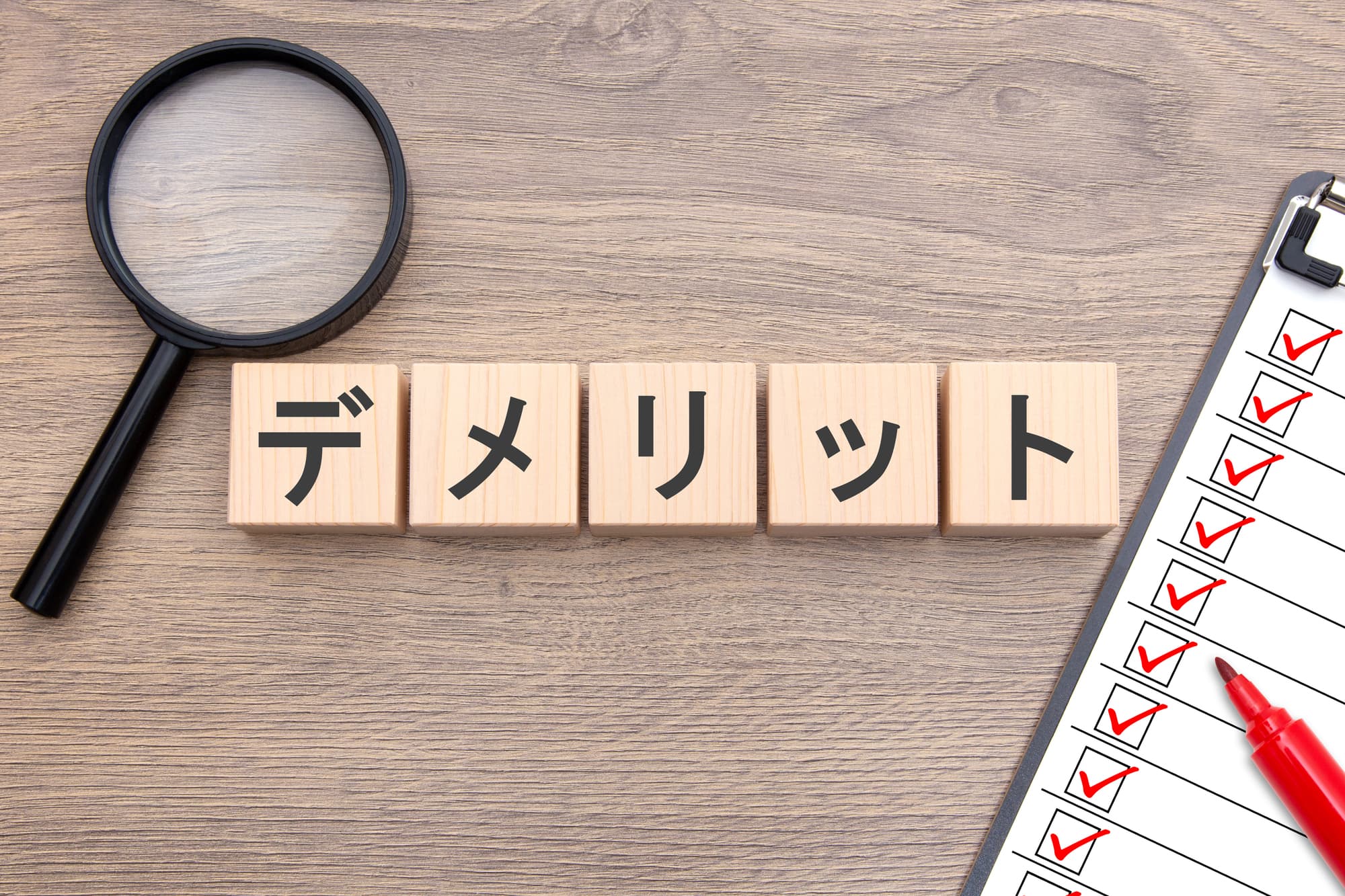 デメリットと書かれたブロックと虫眼鏡、赤ペン、チェックリスト