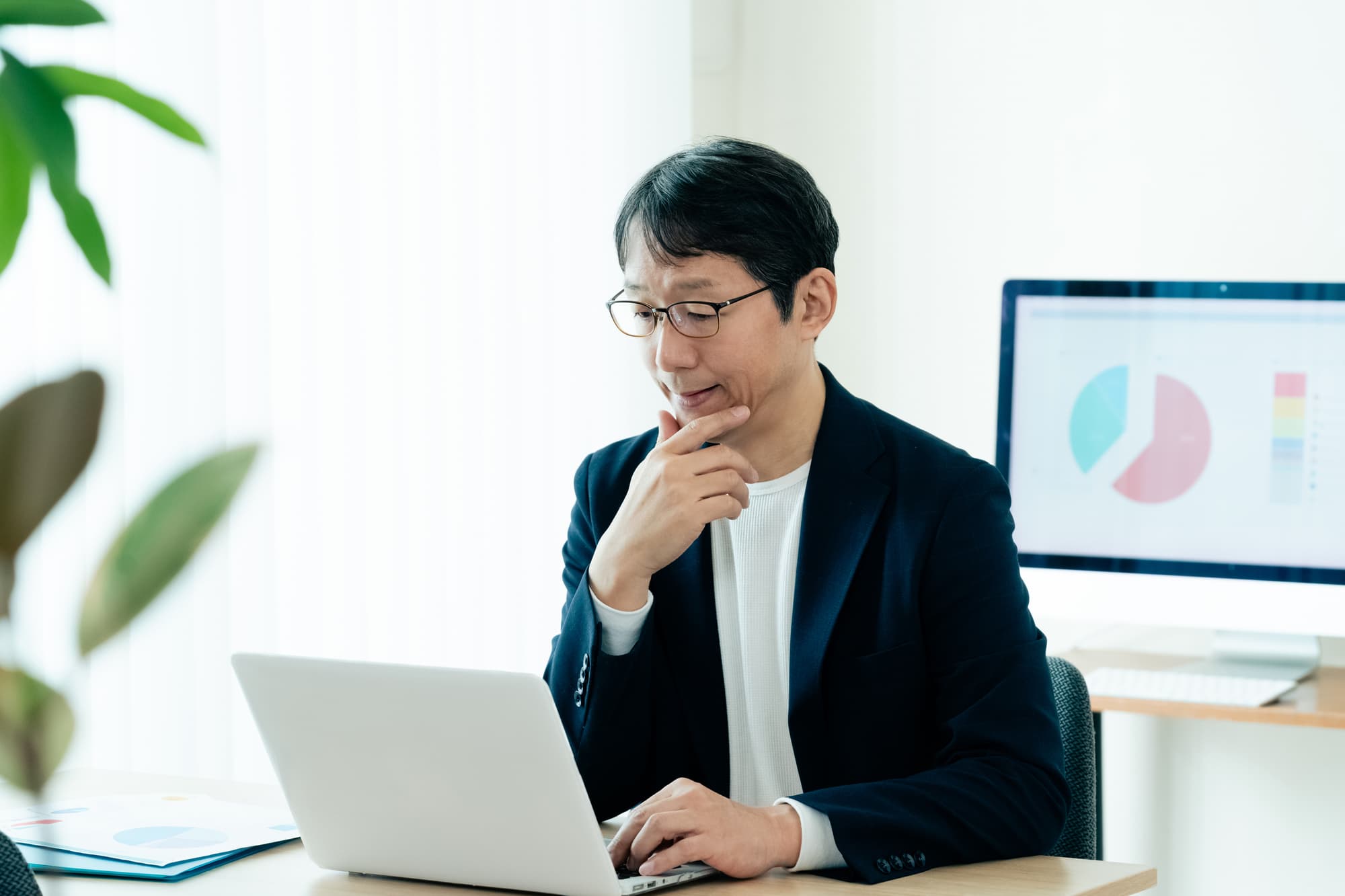 手をあごに当てながらノートパソコンを操作している男性
