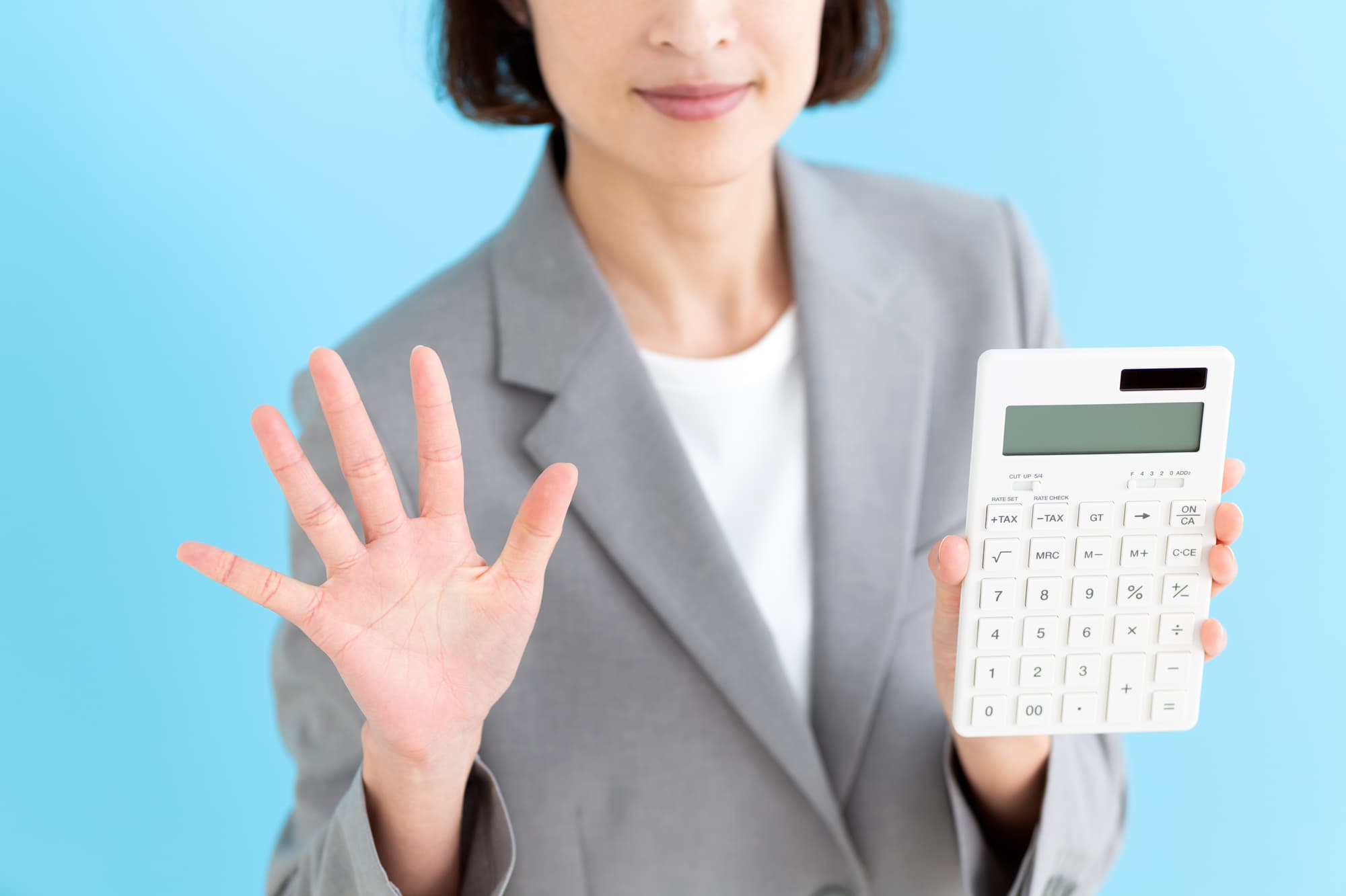 電卓を片手に持ち、もう片方の手で5を示す女性