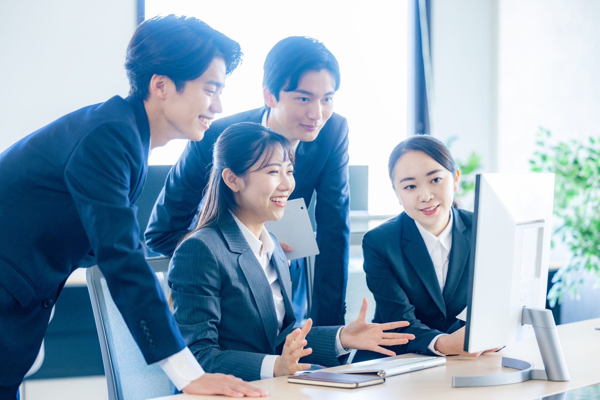 オフィスのパソコン画面をのぞき込み、笑顔を浮かべる4人の男女