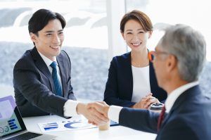 握手をするスーツの男性2人と笑顔の女性