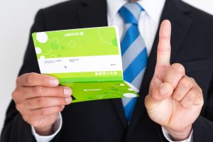通帳を手に持って人差し指を上に向けるスーツ姿の男性