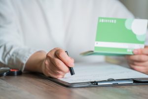 通帳を手に持って書類に印鑑を押す人