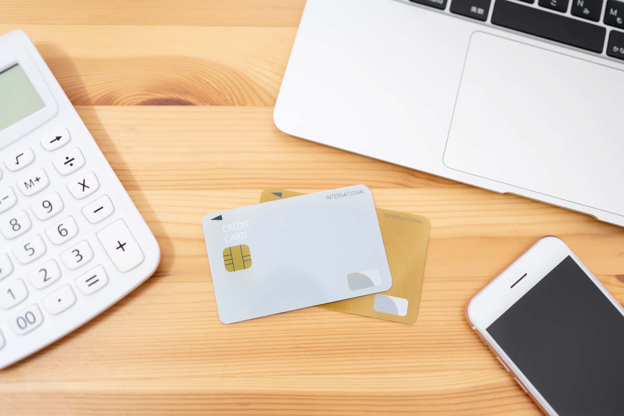机に置かれたキャッシュカードと電卓、ノートPC、スマホ