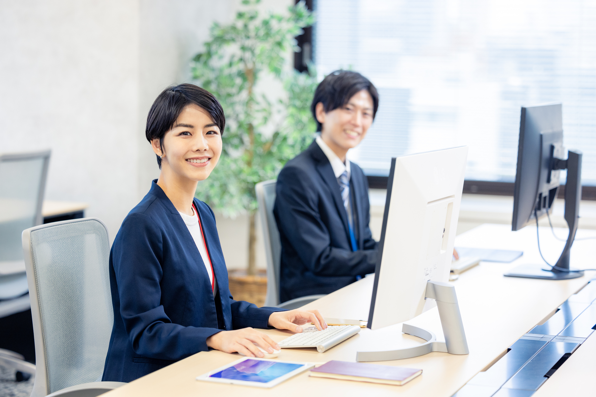 オフィスでPCを操作しながら笑顔を浮かべる男女