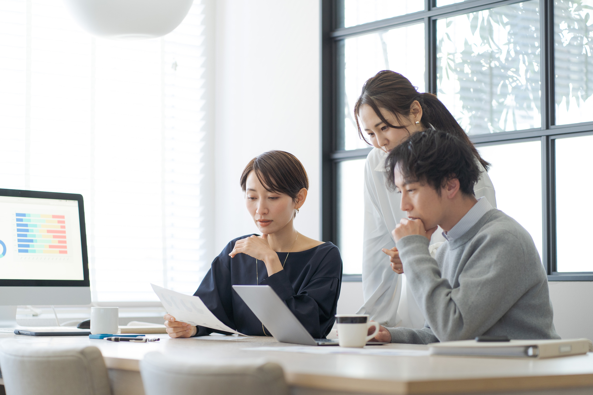 資料を見ながら相談する3人のビジネスパーソン