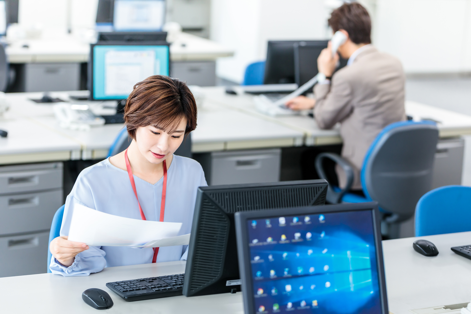 会社のパソコンの前で資料を見ている女性