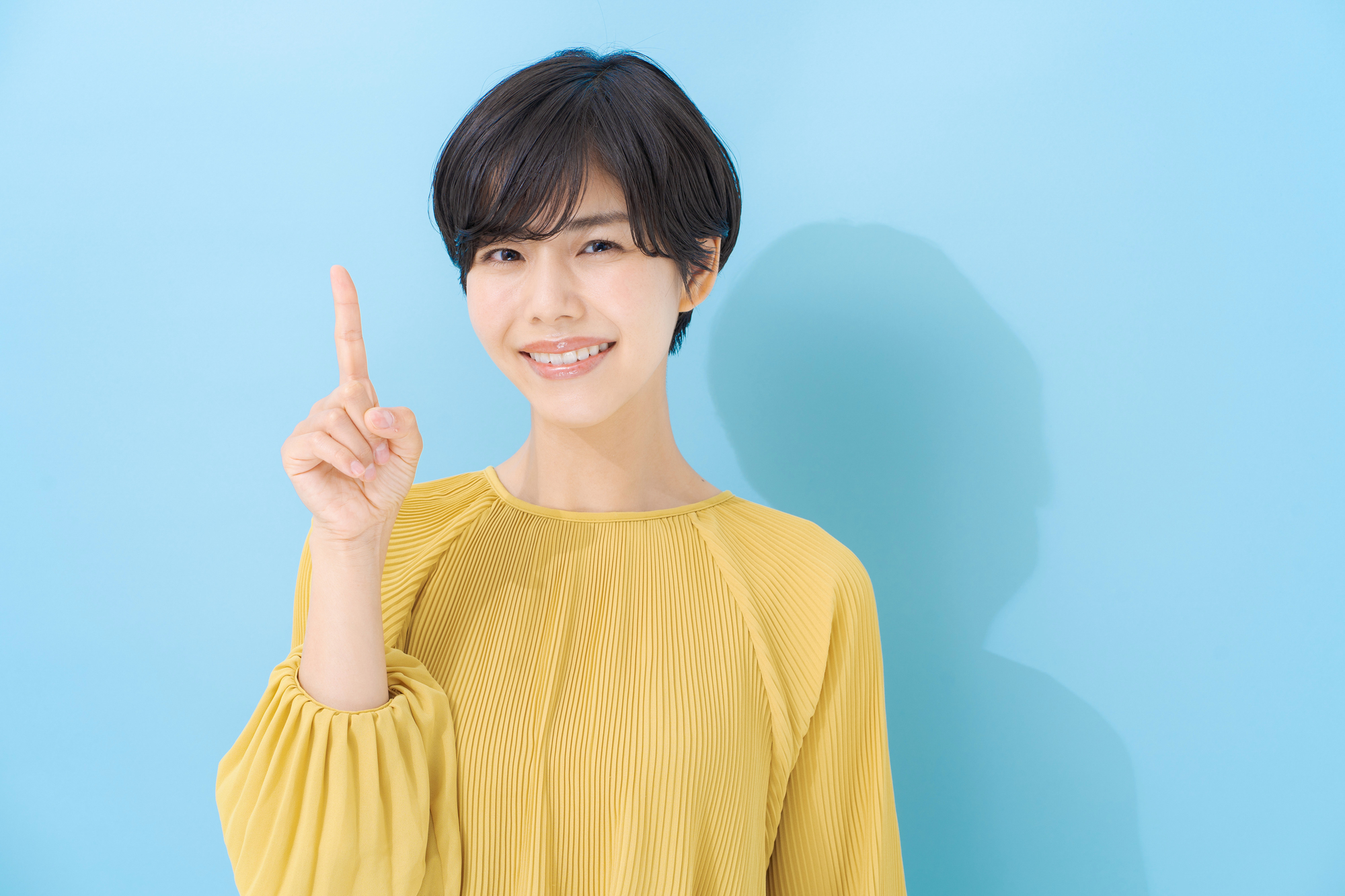 人さし指を立て、こちらを見る笑顔の女性
