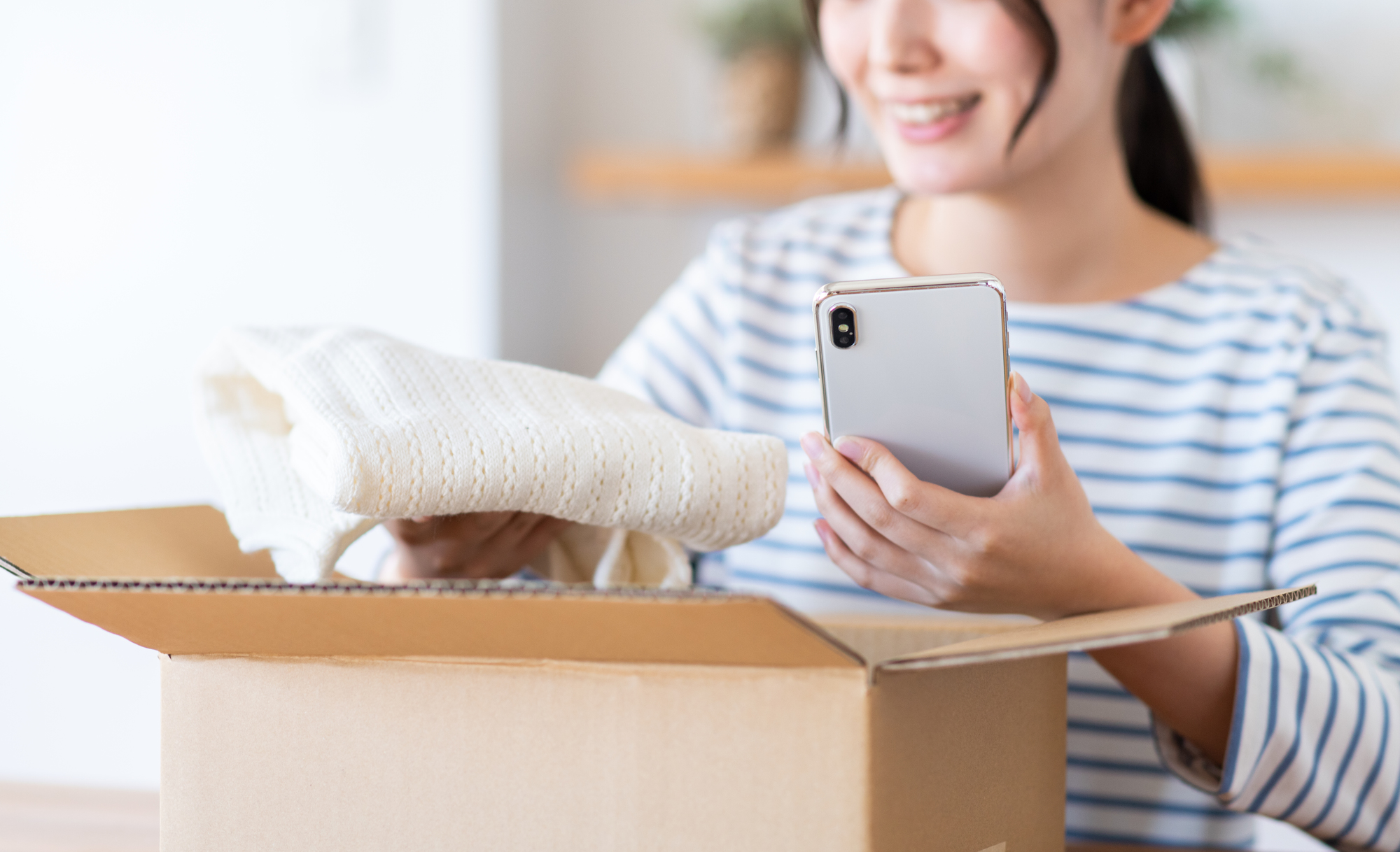 スマホを片手に段ボールから商品を取り出す女性