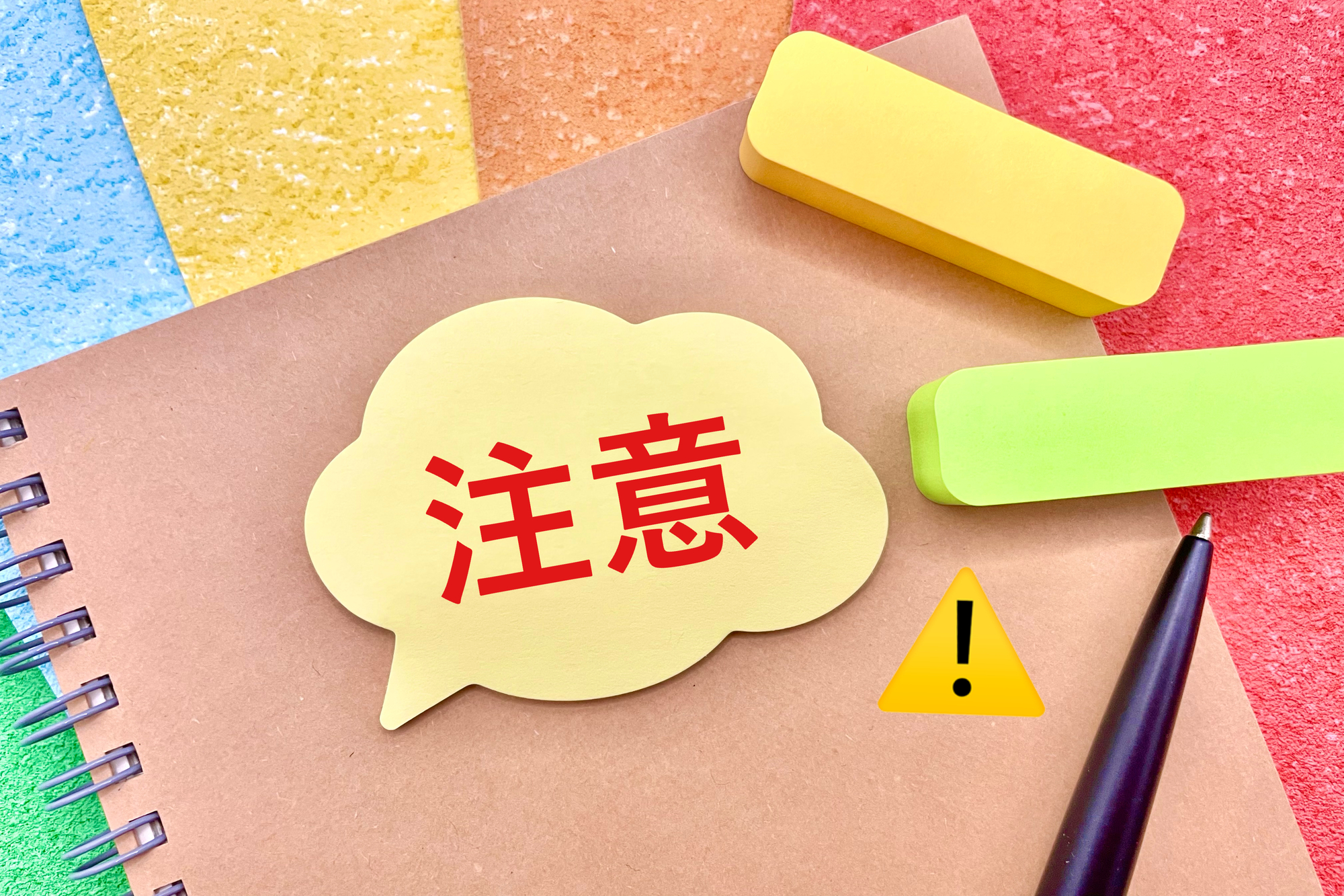 「注意」と書かれた吹き出しとノート、ボールペン、付箋
