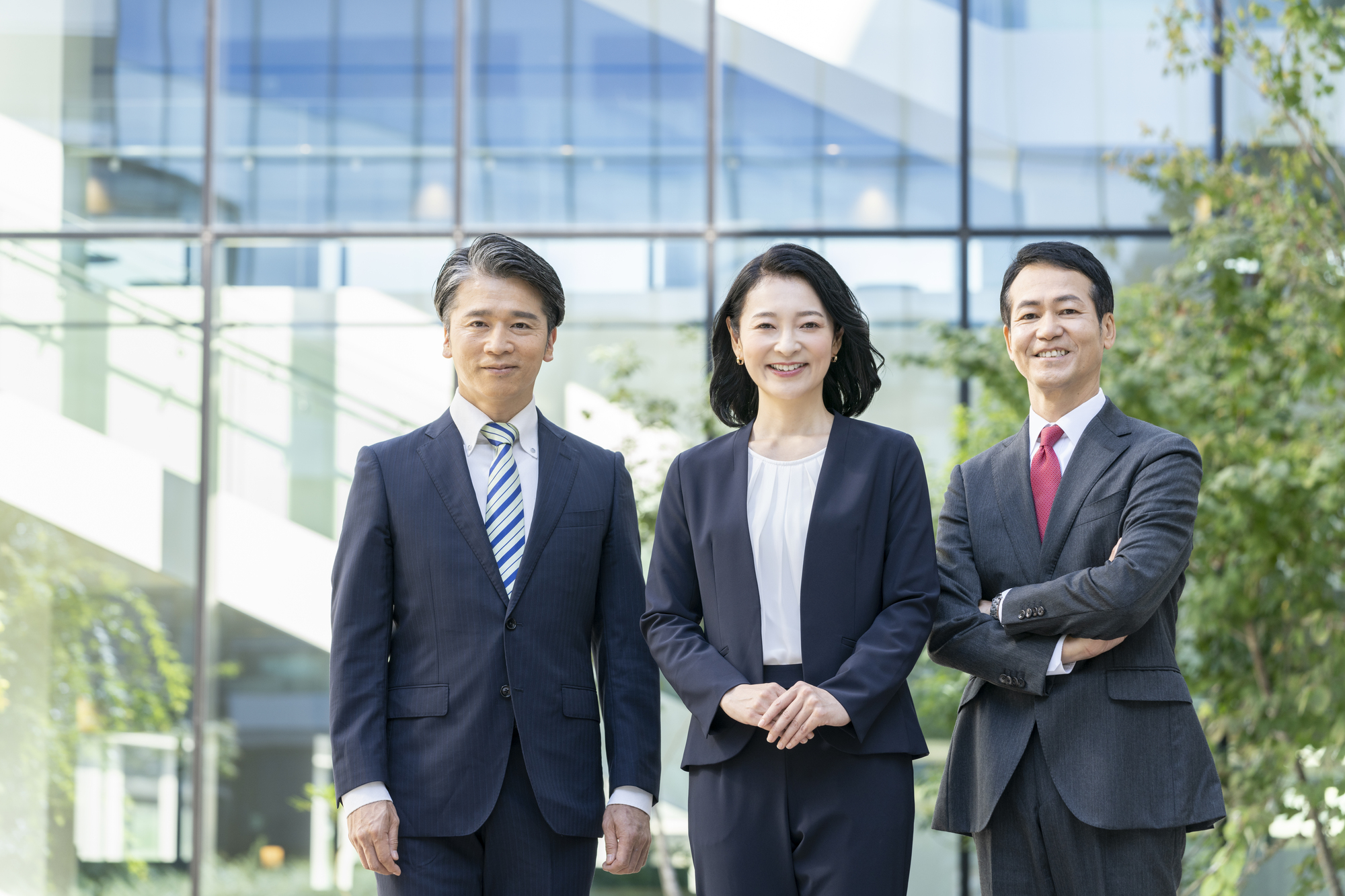 オフィスを背に笑顔を浮かべる3人のビジネスパーソン