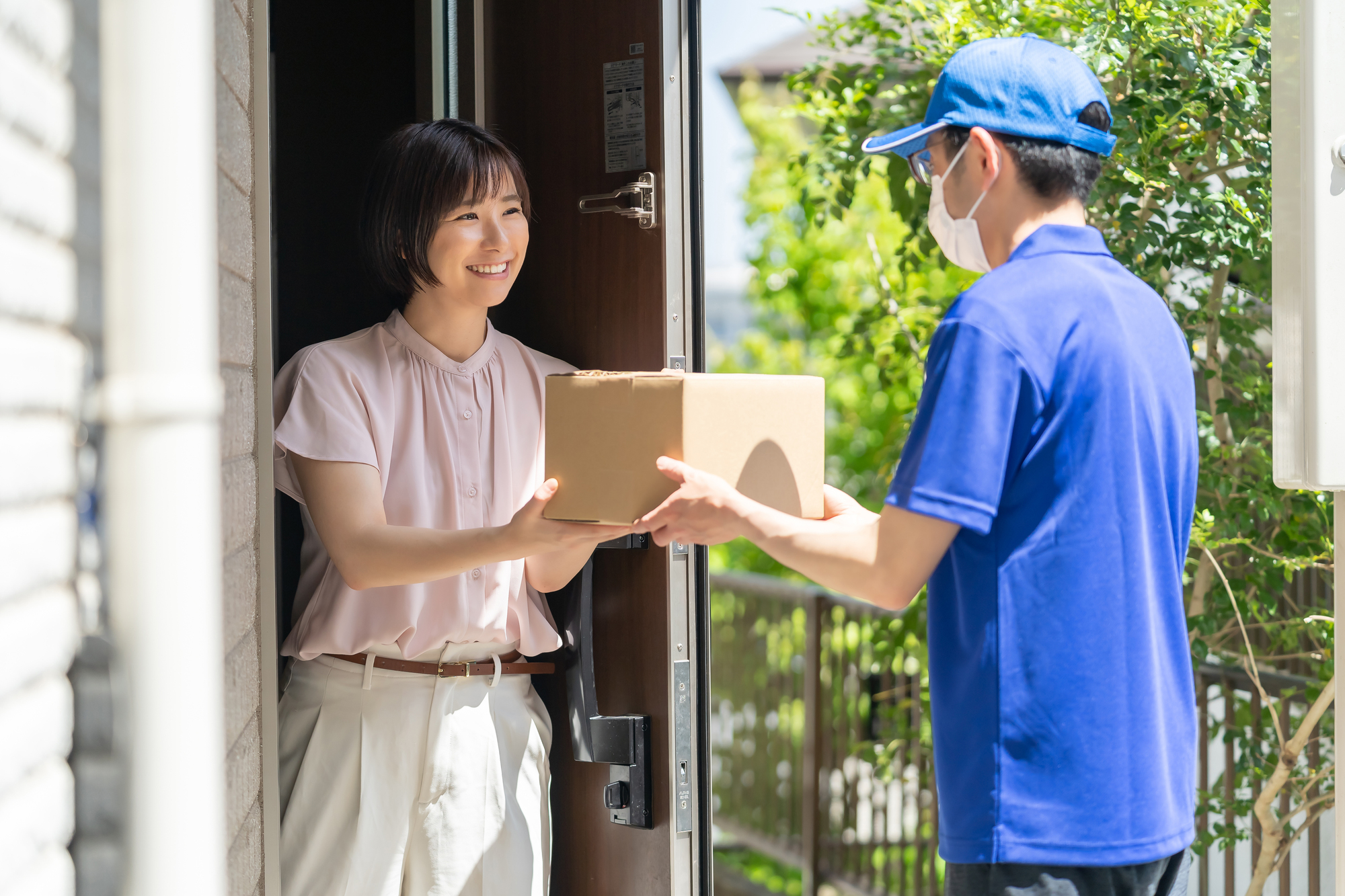 玄関先で配達員から荷物を受け取る女性