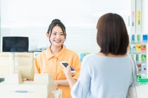 レジで接客するオレンジの服を着た女性と、スマホを持つ女性の後ろ姿
