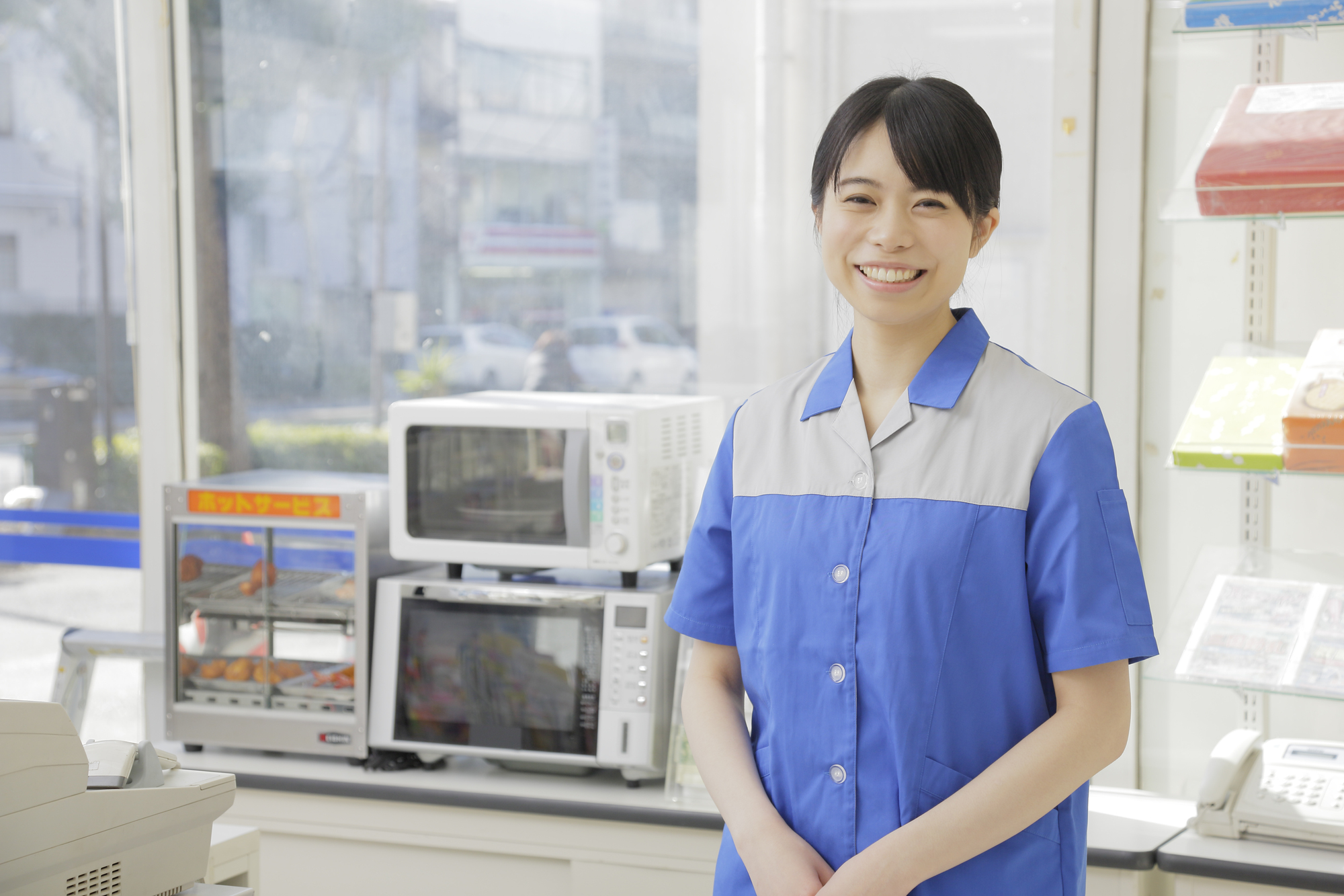 レジの前で両手を組む笑顔のコンビニ店員