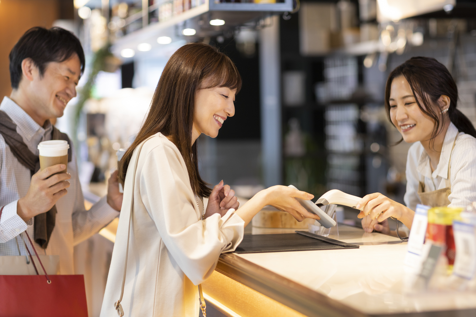 スマホの画面を提示する女性客、スキャナーで読み込む女性店員