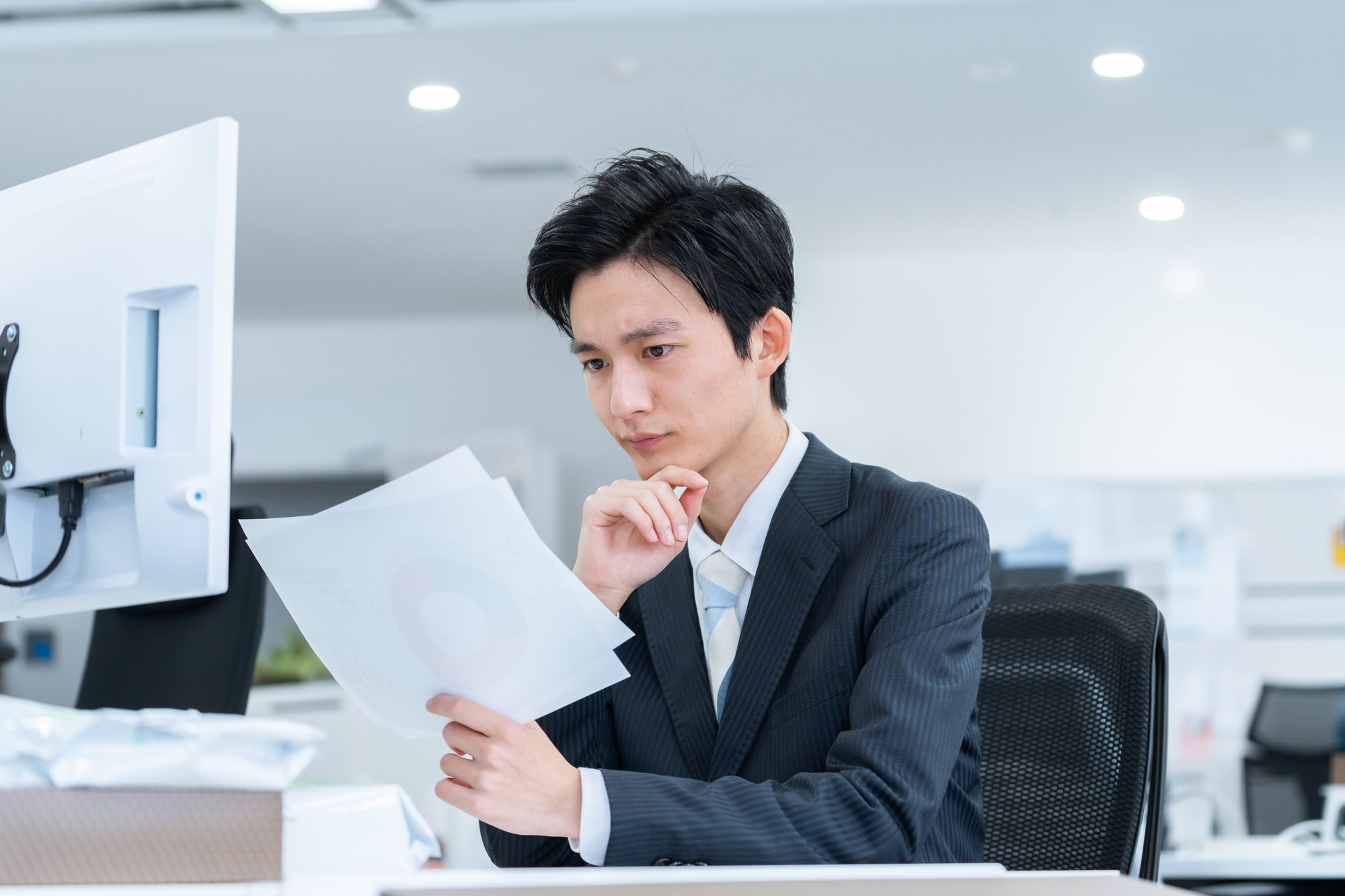 パソコンの前で資料を見ながら考え事をしている男性