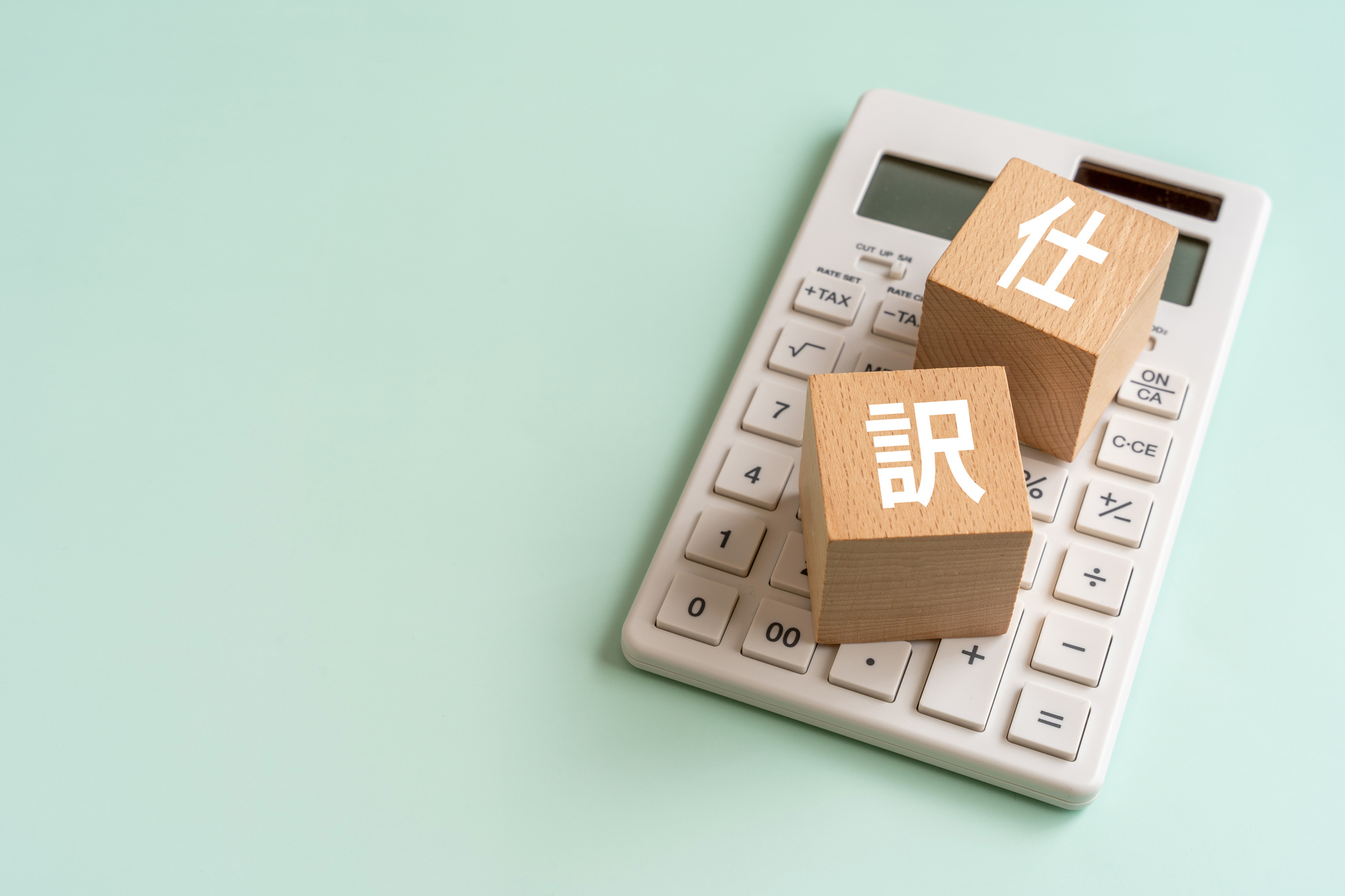 電卓と「仕訳」と書かれた木のブロック