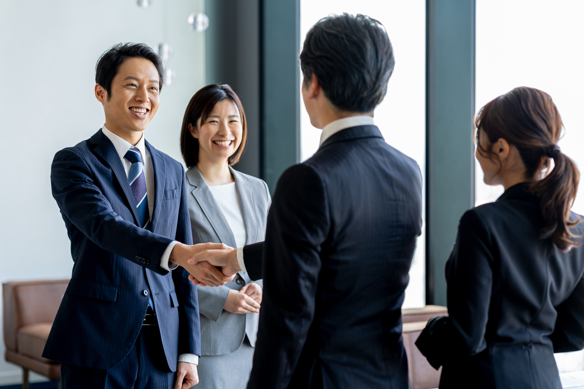 握手している2人のビジネスパーソンと、笑顔の女性2人