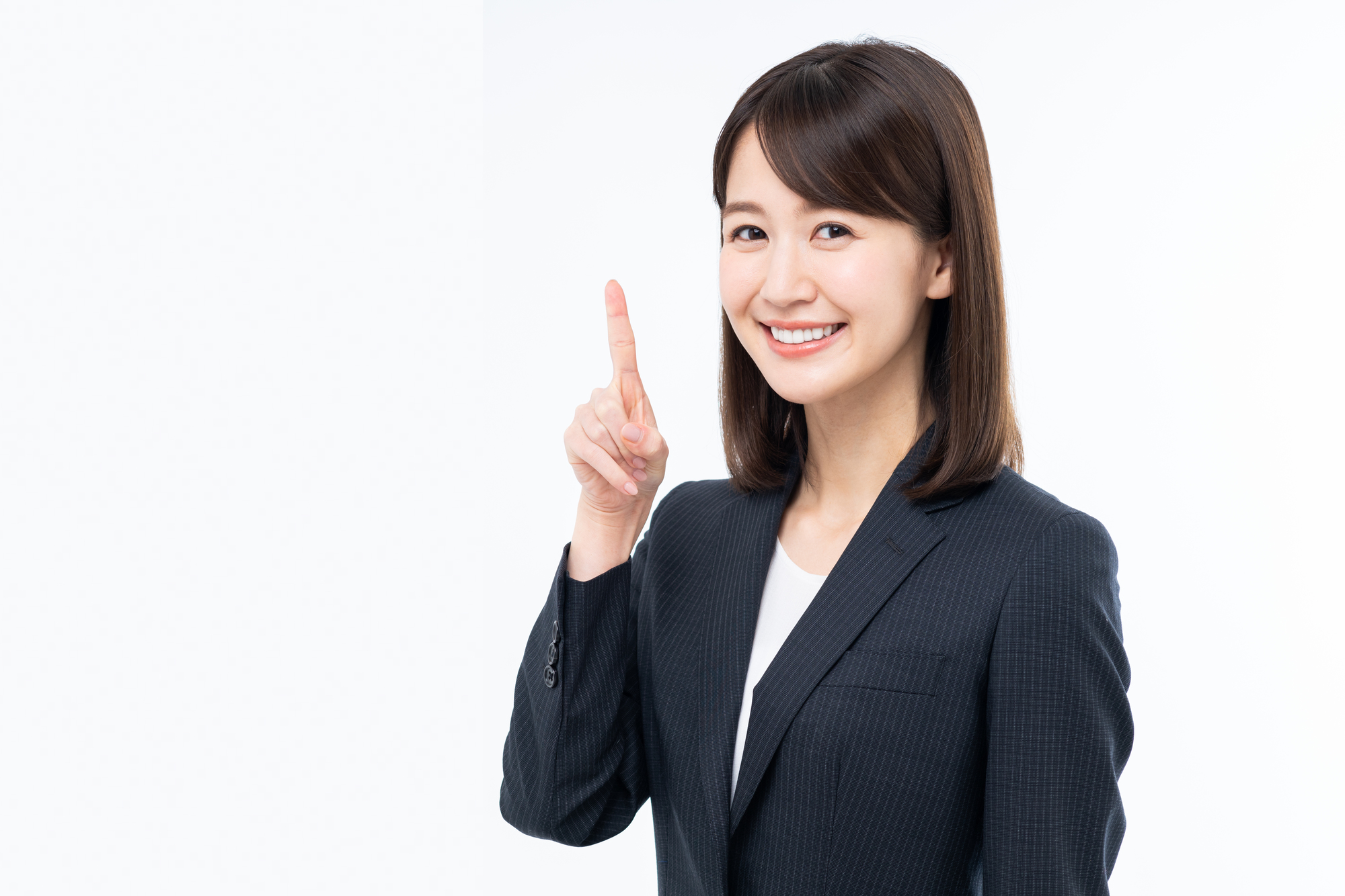 右手の人さし指を立て、笑顔でこちらを見るスーツの女性
