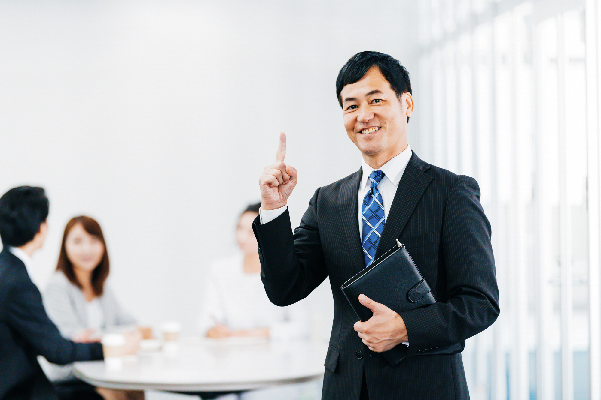 手帳を片手に、人さし指を上に向けている笑顔のビジネスパーソン
