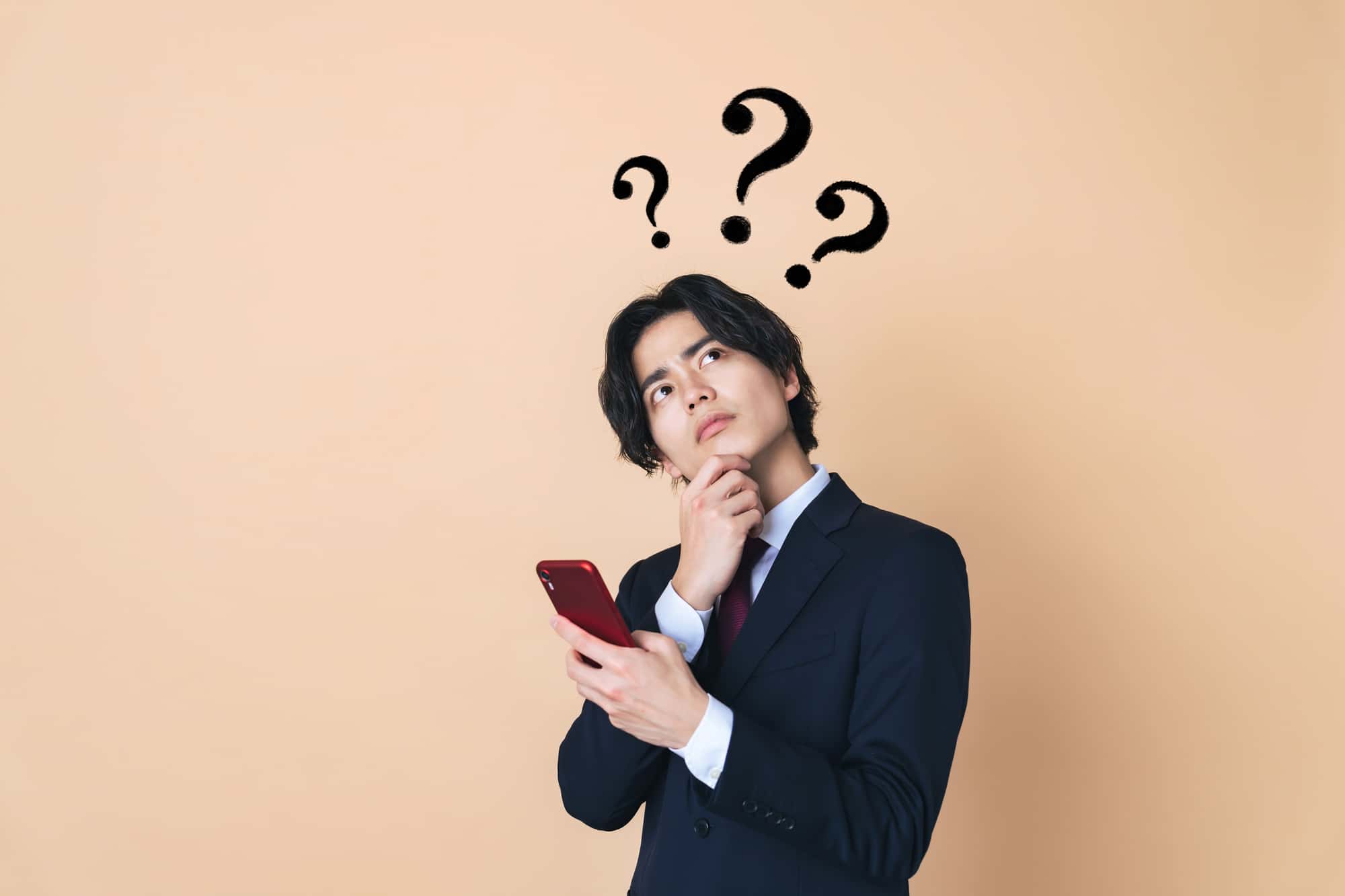 スマートフォンを手に持ち、疑問を浮かべるビジネスパーソン