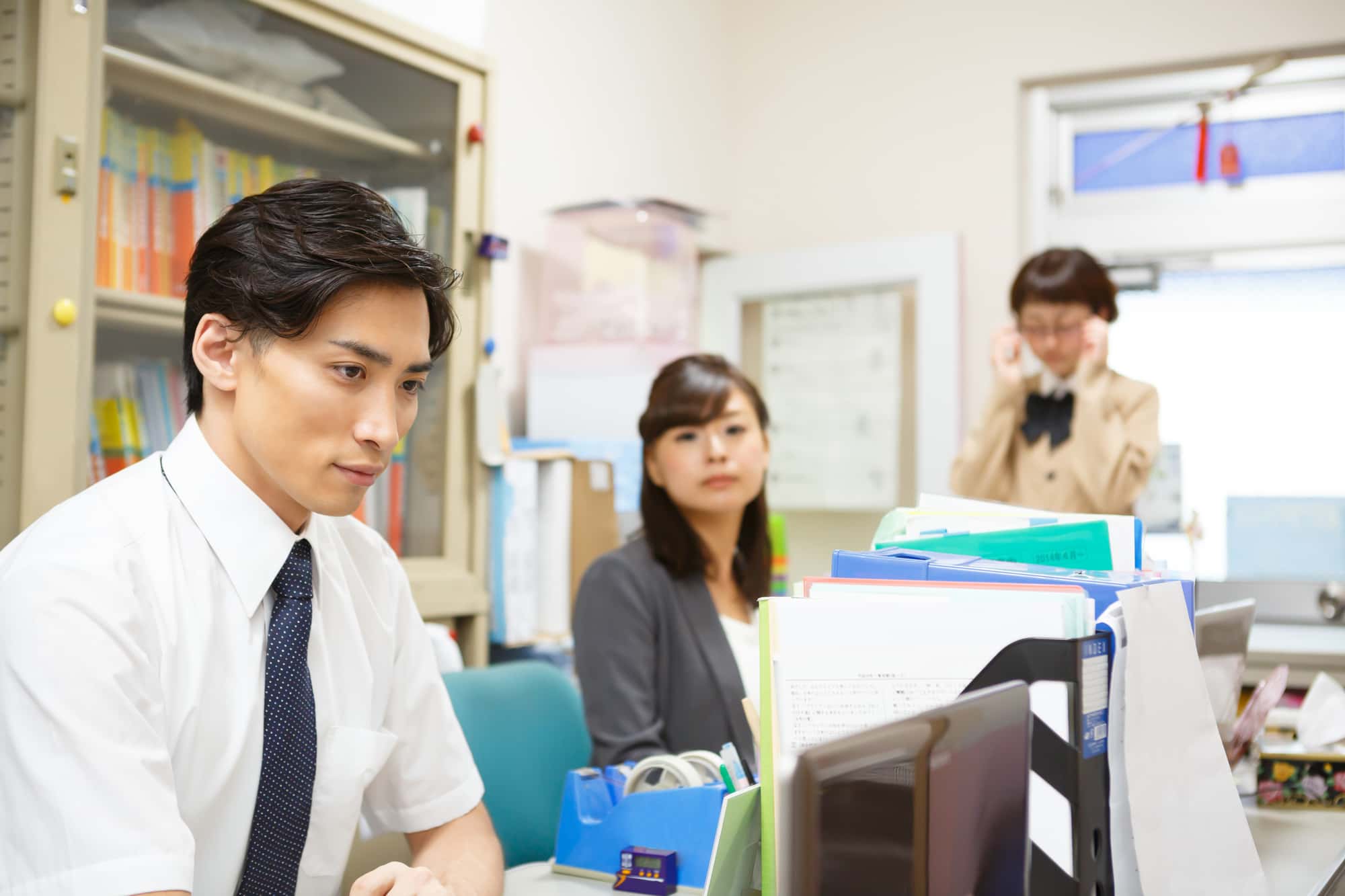職員室で仕事をしている3人の教員