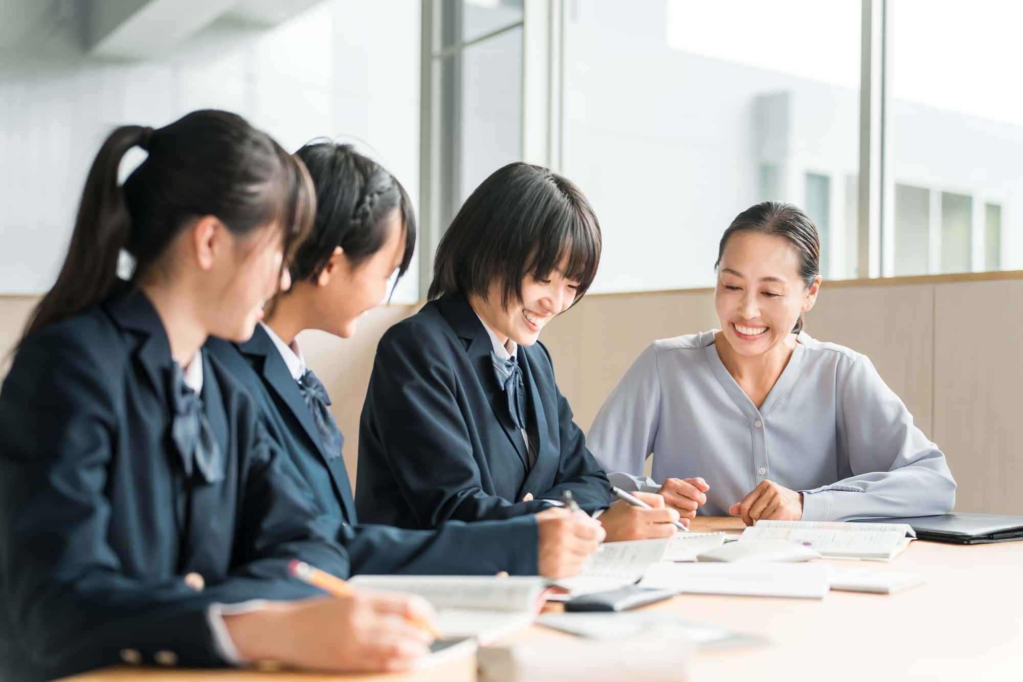 笑顔で勉強をする3人の女子生徒と教員