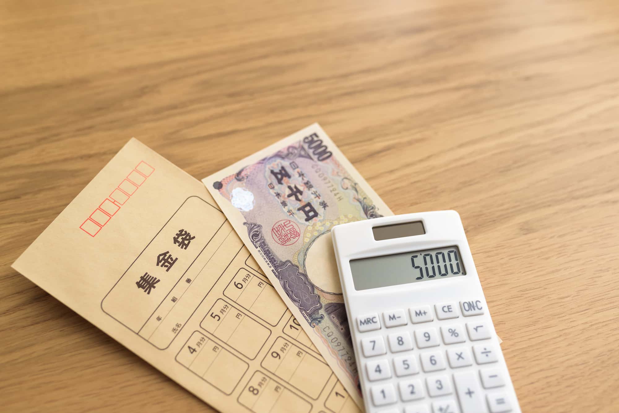 机の上に置かれた集金袋と5,000円紙幣、電卓