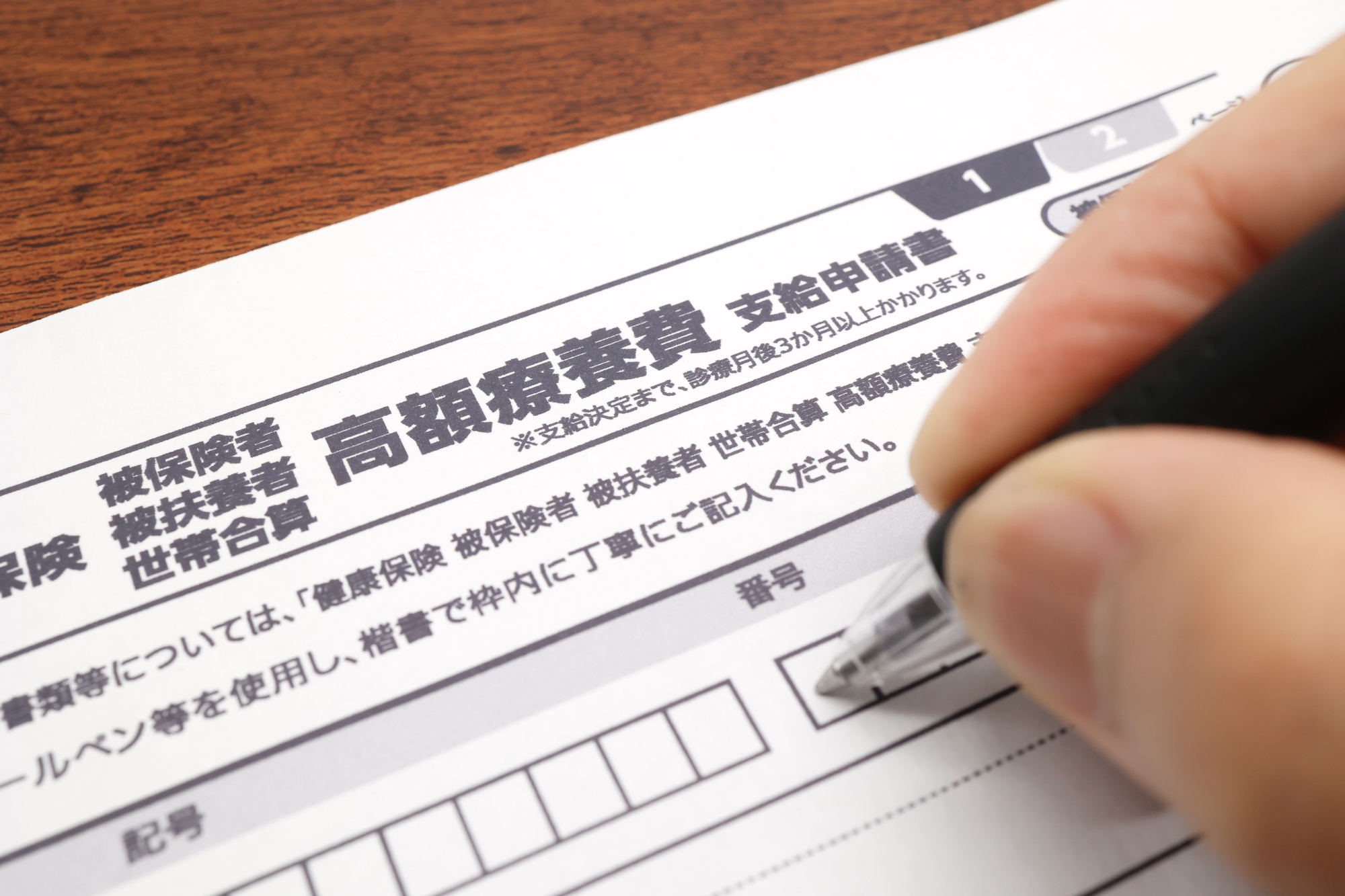 高額療養費支給申請書に記入している人の手元とボールペン
