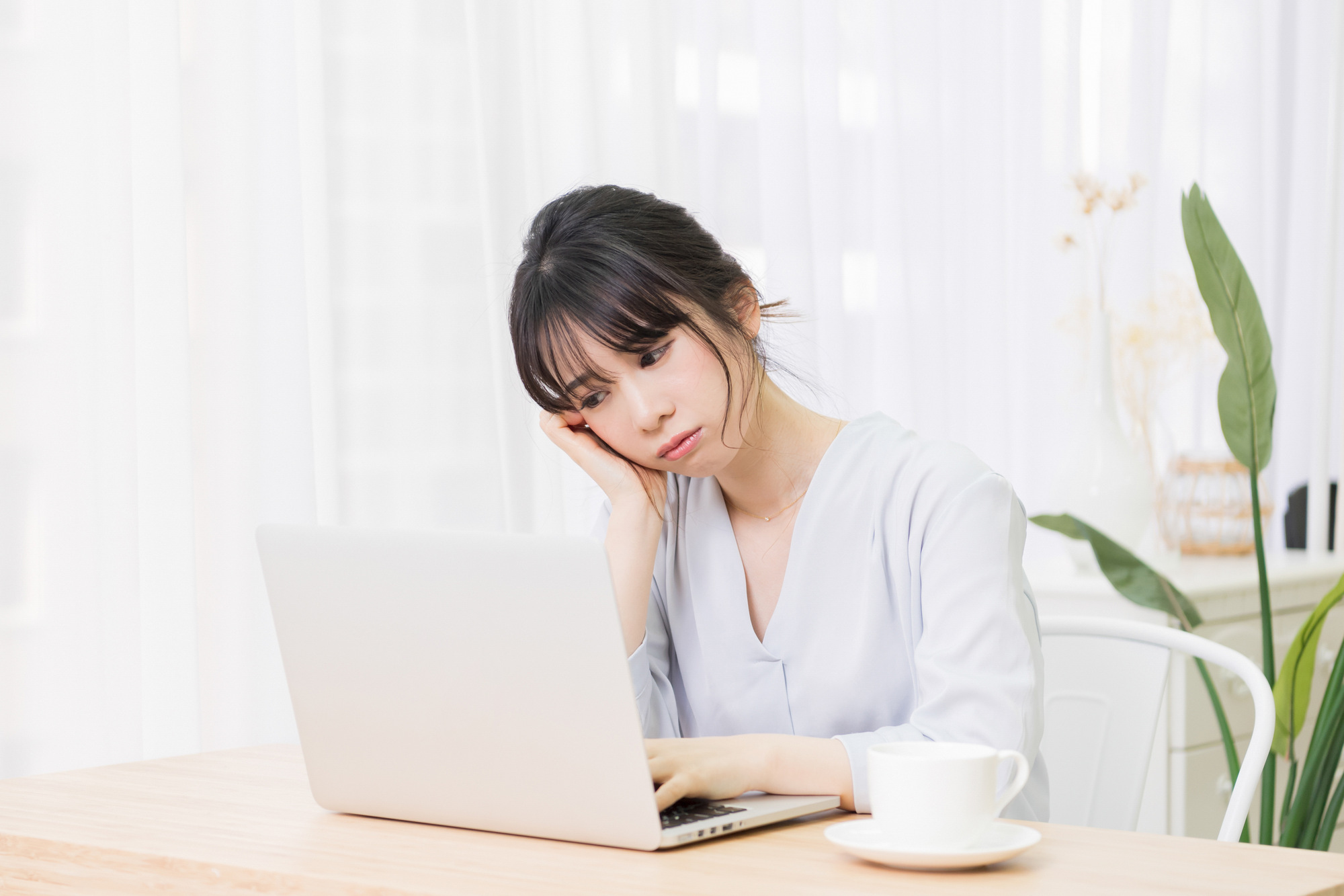 ノートパソコンの前で悩む女性
