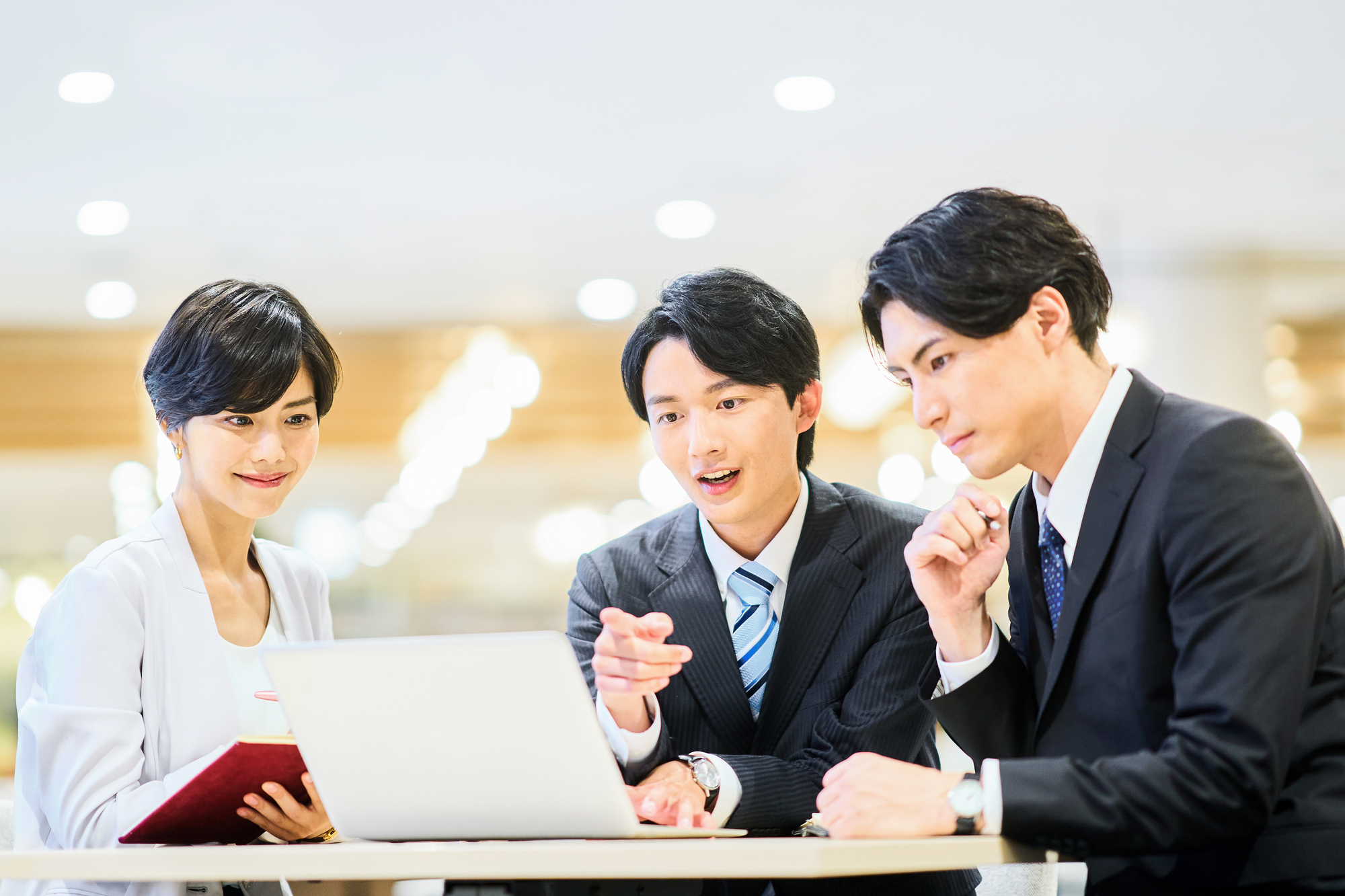 ノートパソコンを見ながら会議をする3人のビジネスパーソン