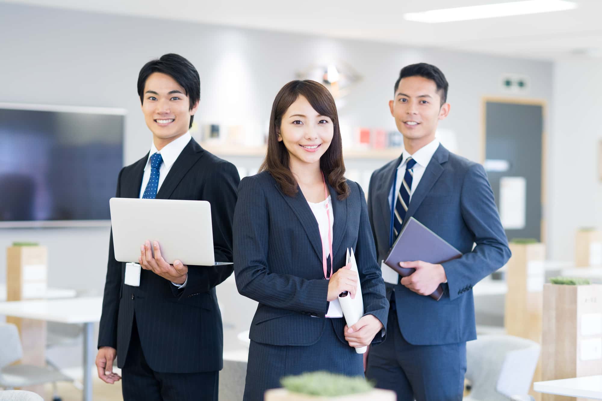 オフィスで笑顔を浮かべる3人のビジネスパーソン