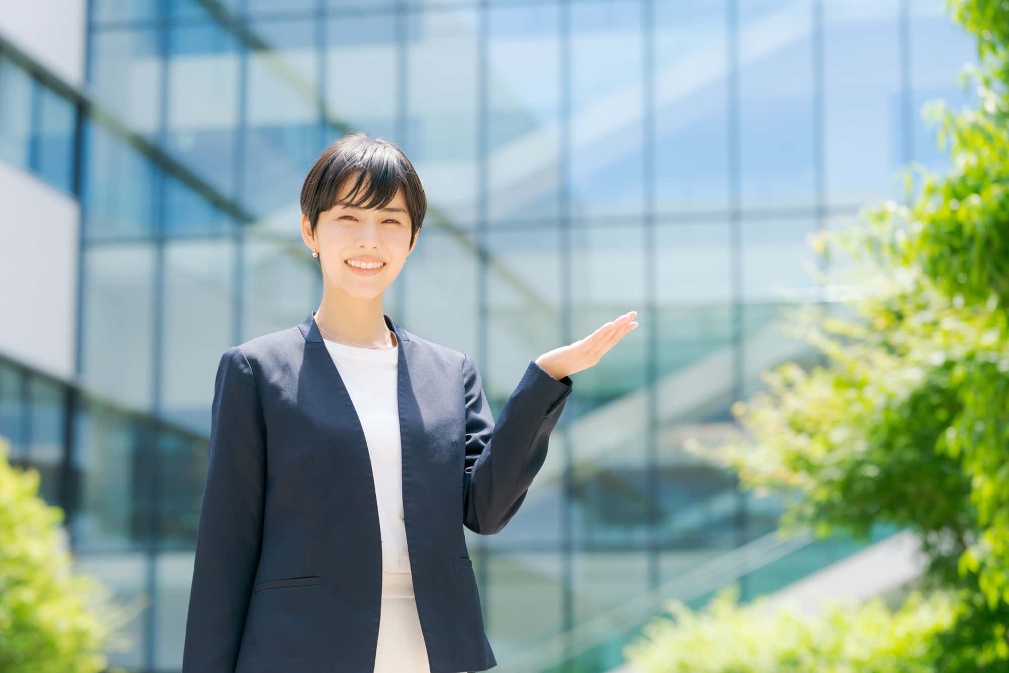 ビルの前で案内をする笑顔の女性