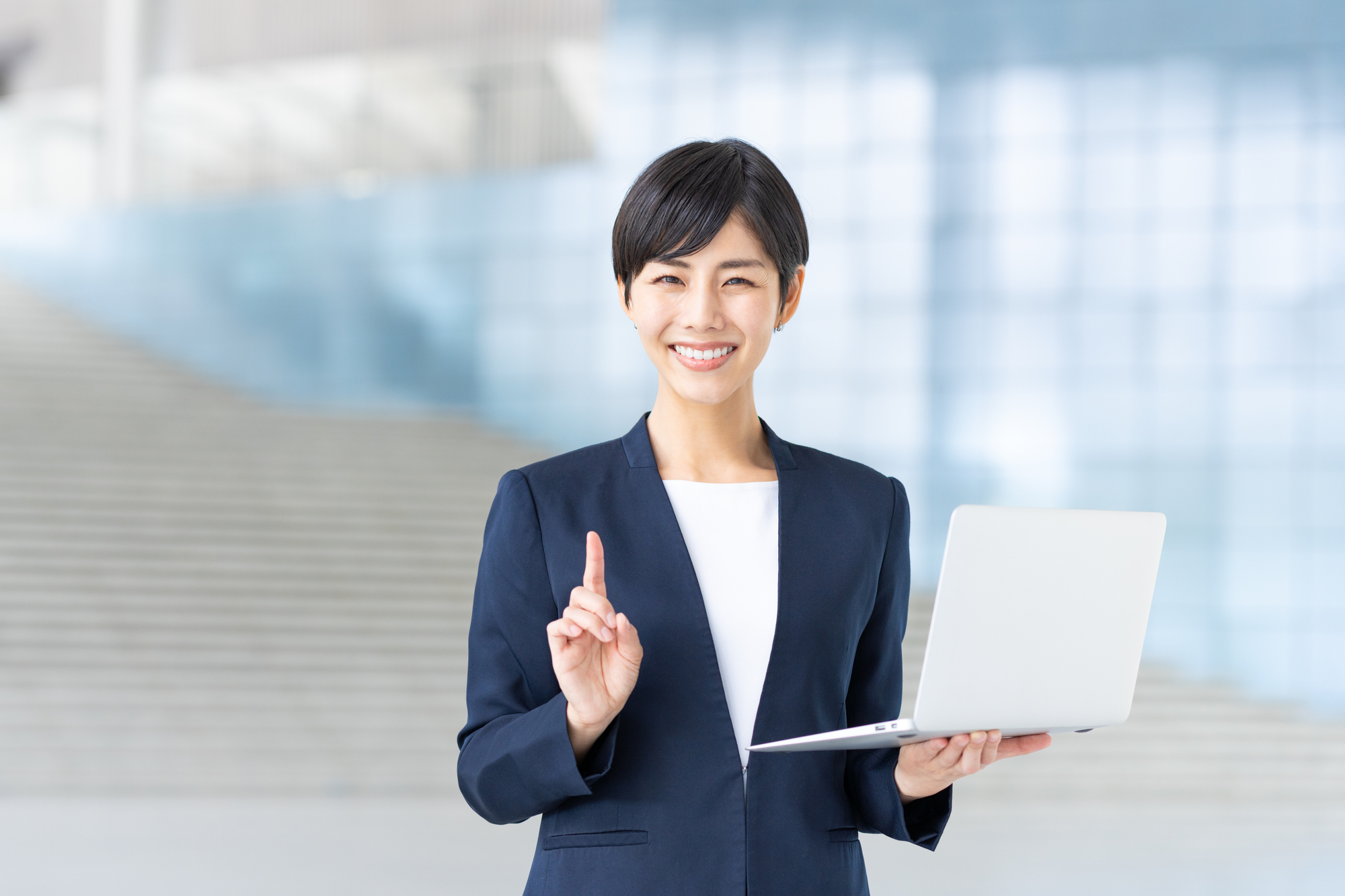 ノートパソコンを片手に、笑顔で説明をする女性