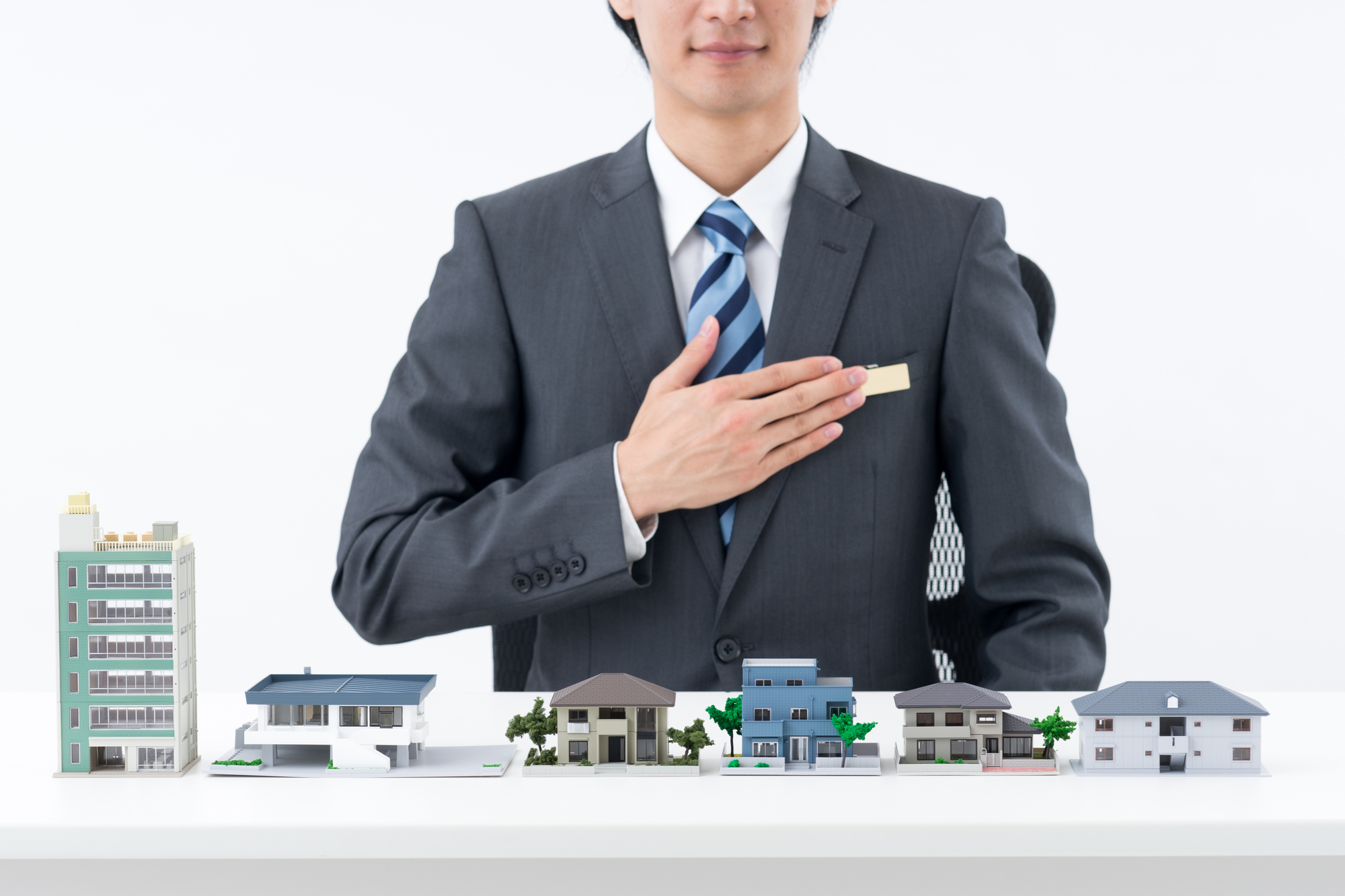 いくつかの建物の模型と、手を胸に当てて自信を示すビジネスパーソン