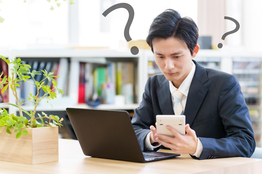 電卓を片手にクエスチョンマークを浮かべるビジネスパーソン