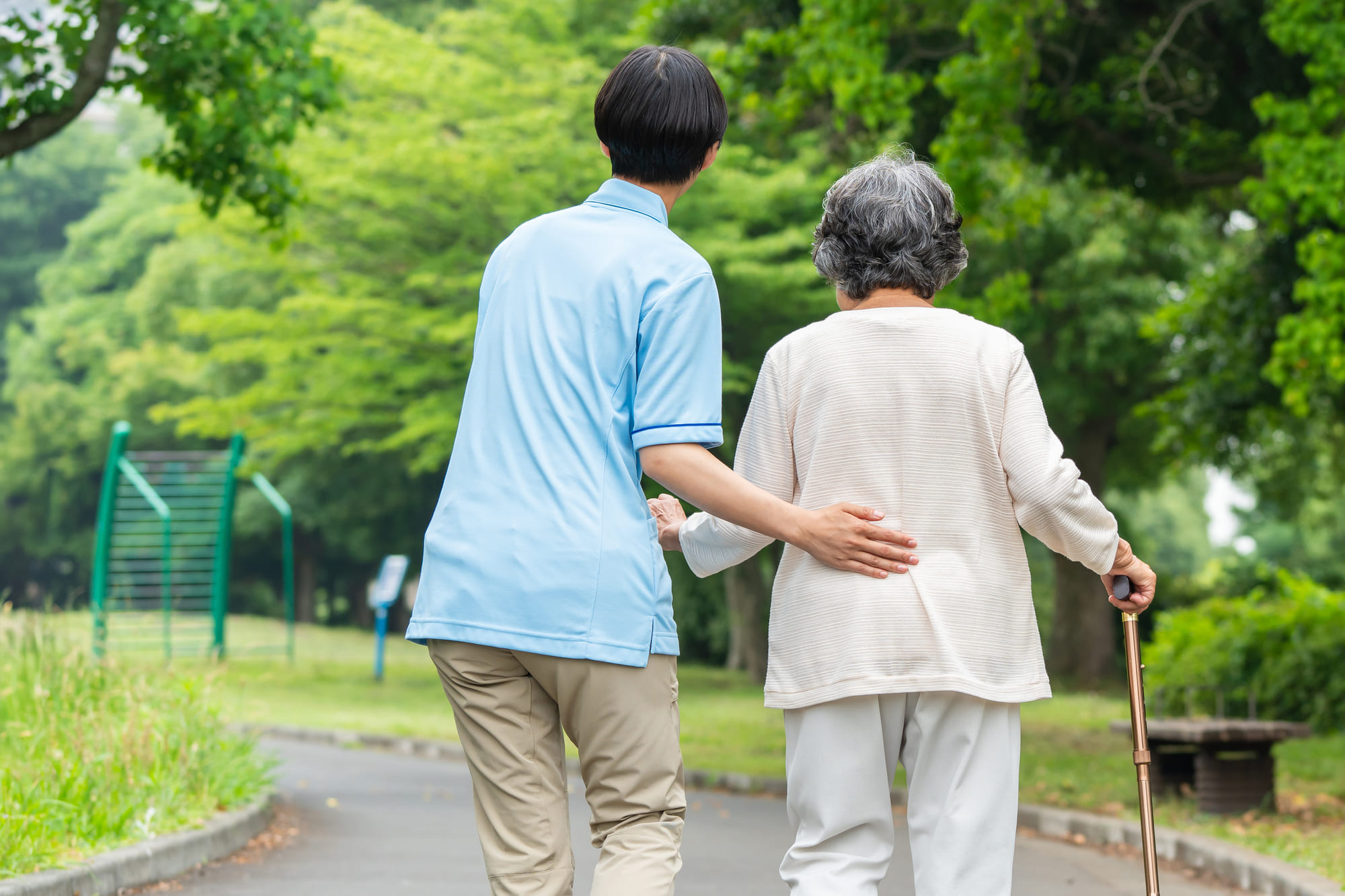 杖を使って歩く女性と、それを支える介護スタッフ