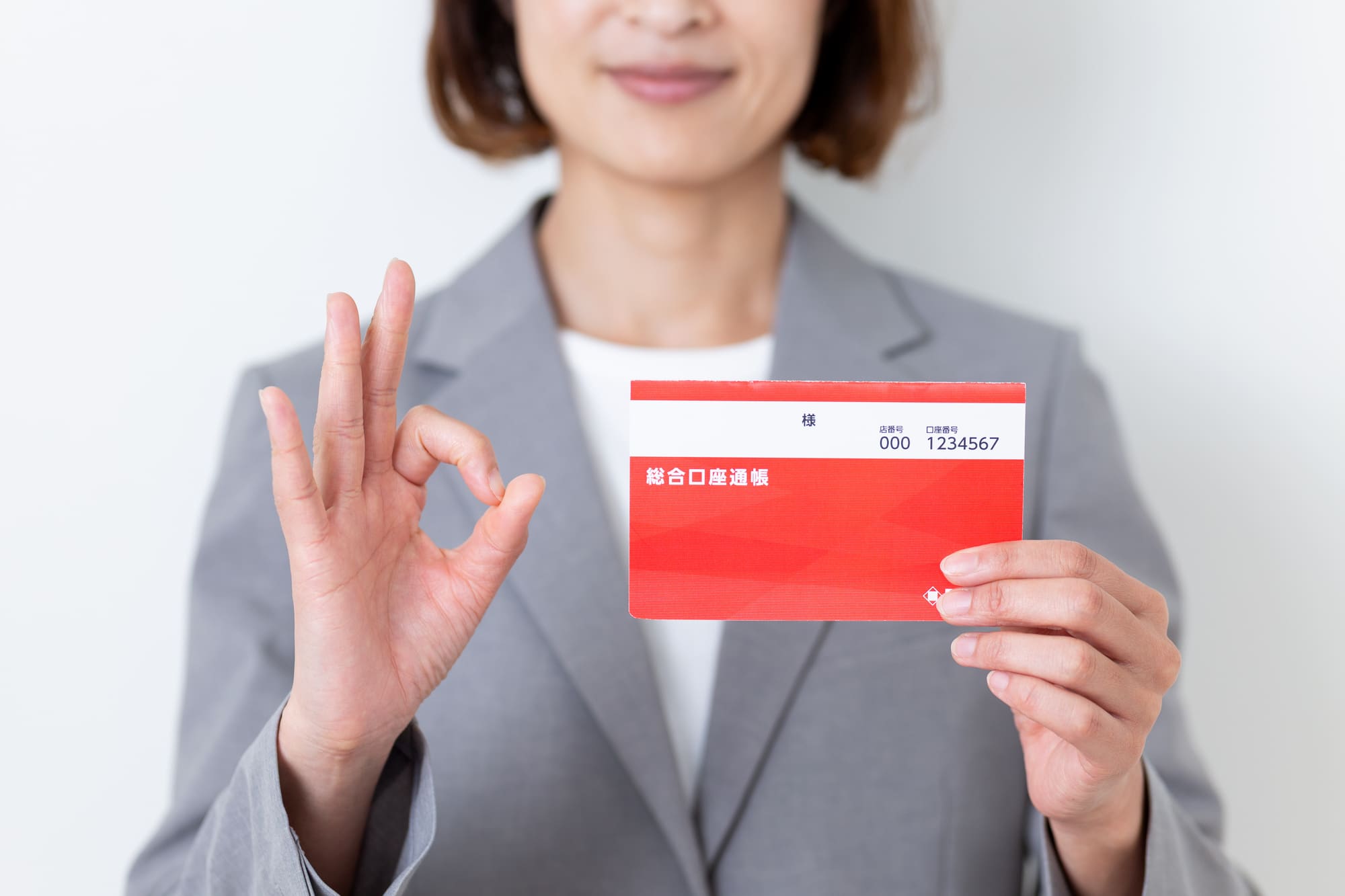 通帳を片手に、手でOKサインを示す女性