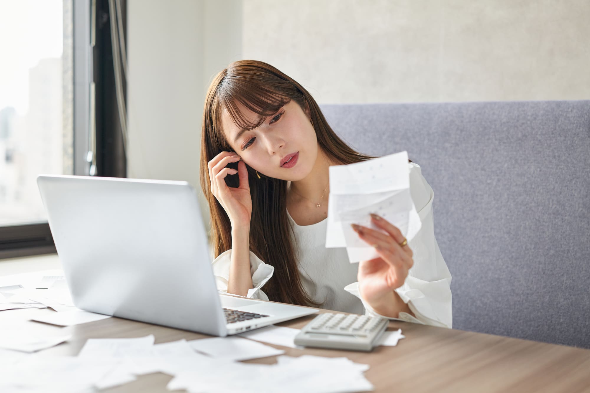 パソコンの前で、書類を片手に悩む女性