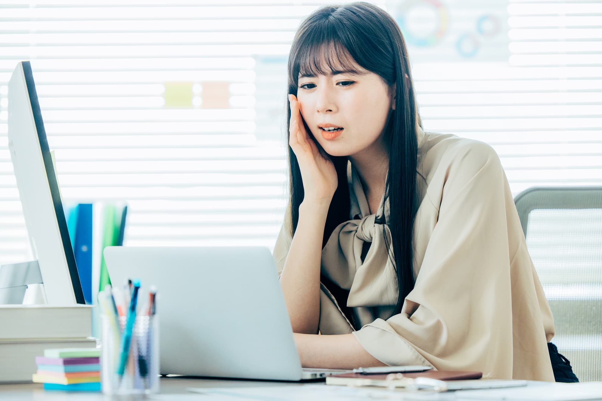 オフィスのパソコンの前で悩んだ表情を浮かべる女性