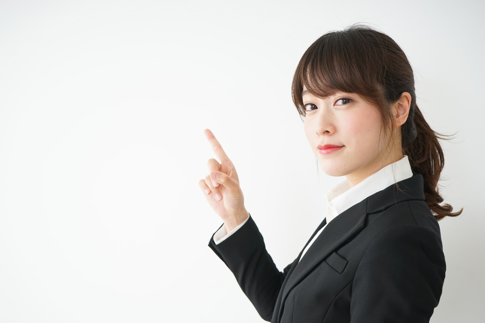 人さし指を上に向け、こちらを見ているスーツ姿の女性