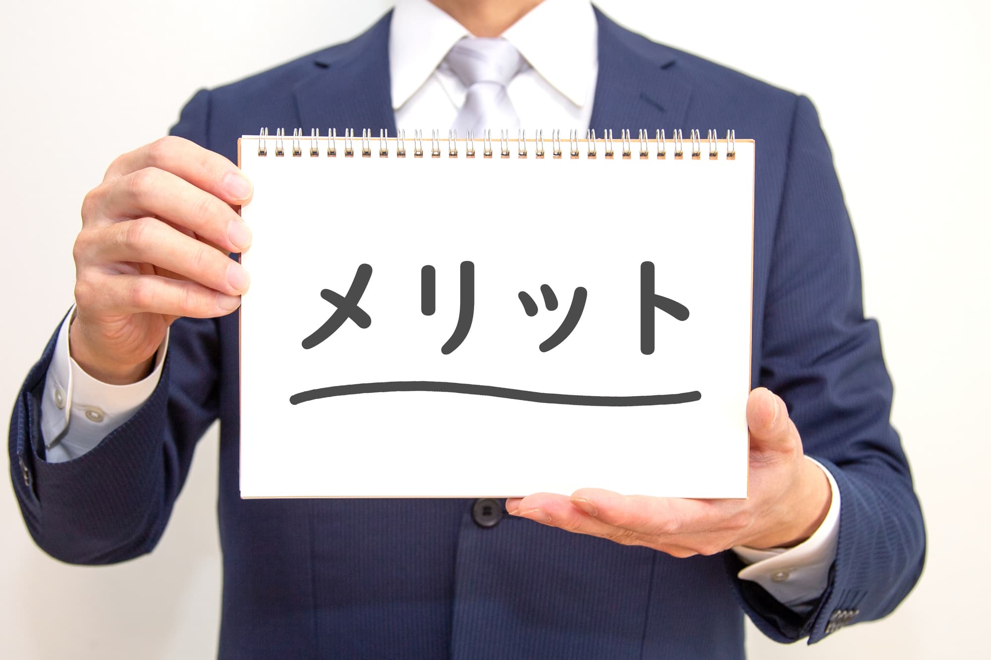 「メリット」と書かれたノートを手に持ったスーツ姿の男性