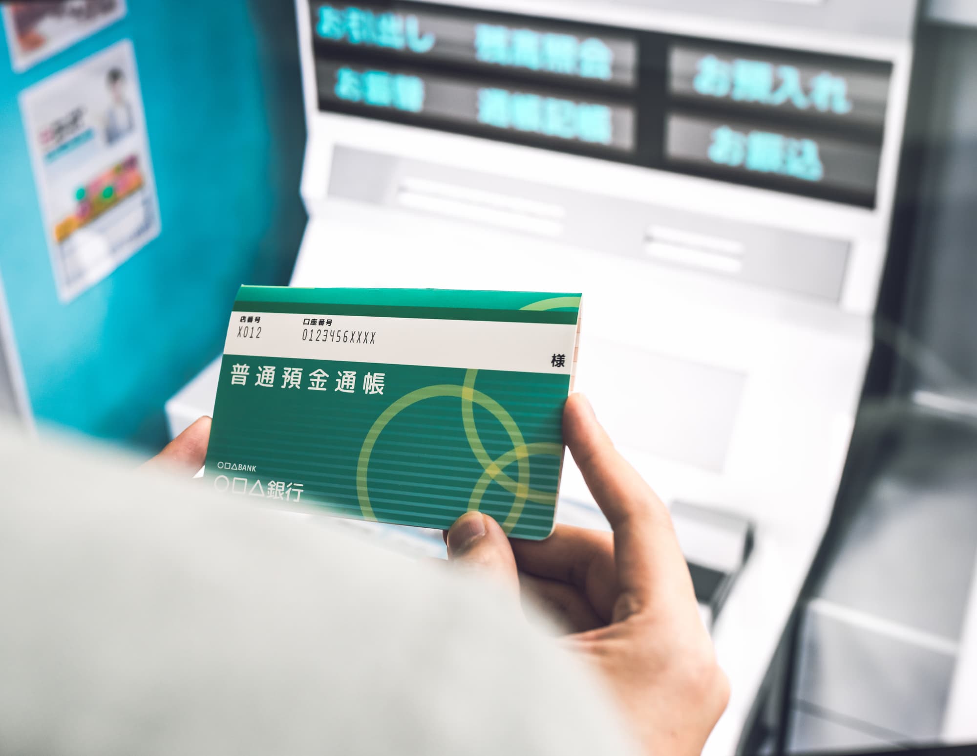 銀行ATMの前で通帳を手にしている人